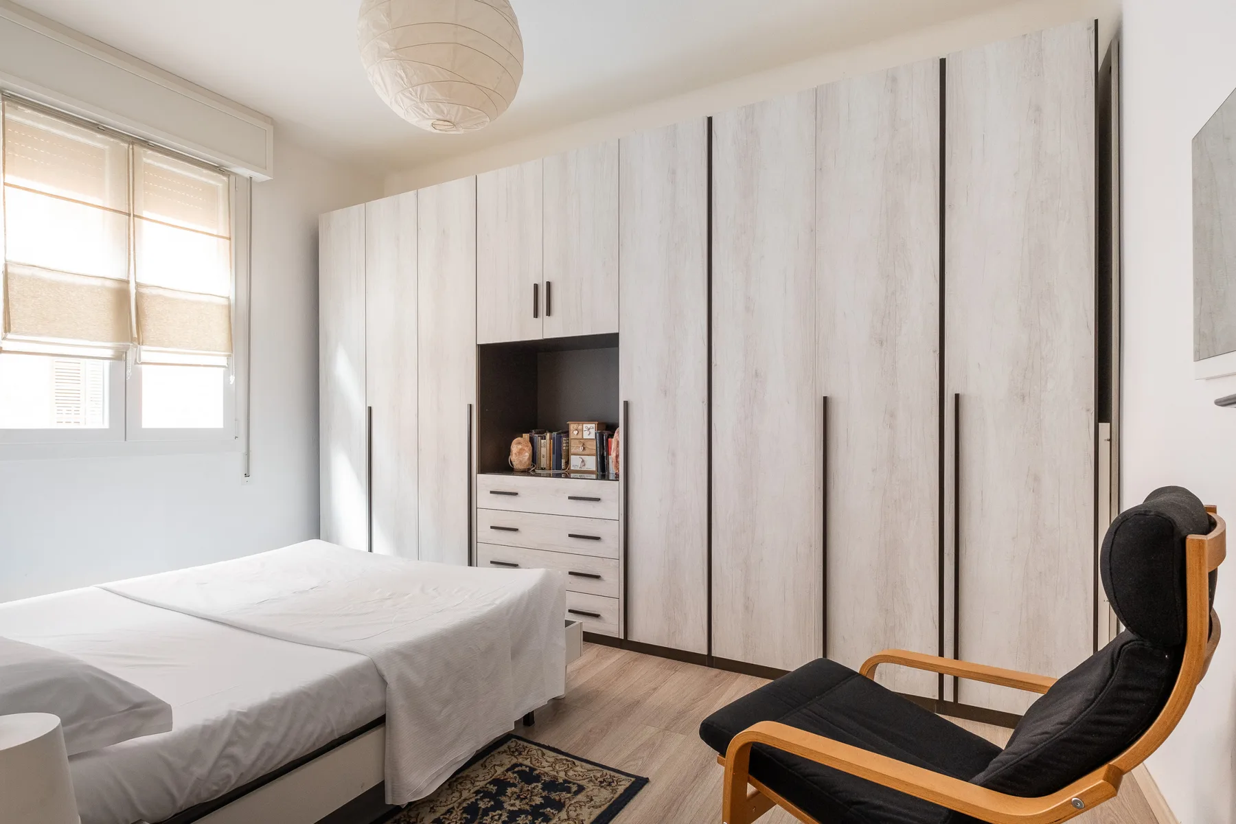 A bedroom with a bed, built-in storage, and a lounge chair.
