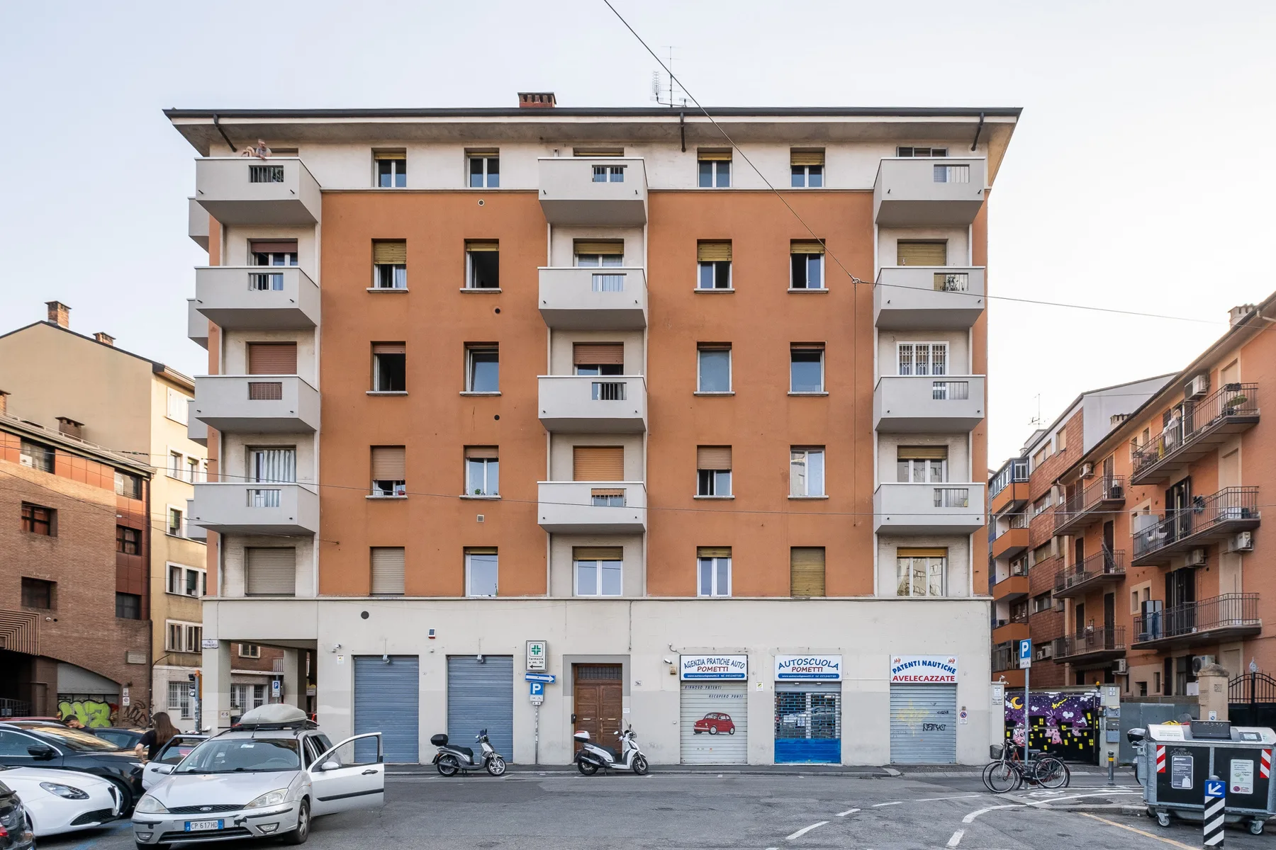 An orange apartment building faces a paved street with parked cars.
