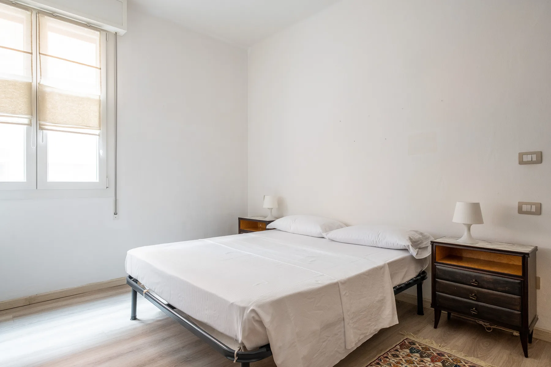 A bright bedroom with a double bed, bedside tables, and a window.