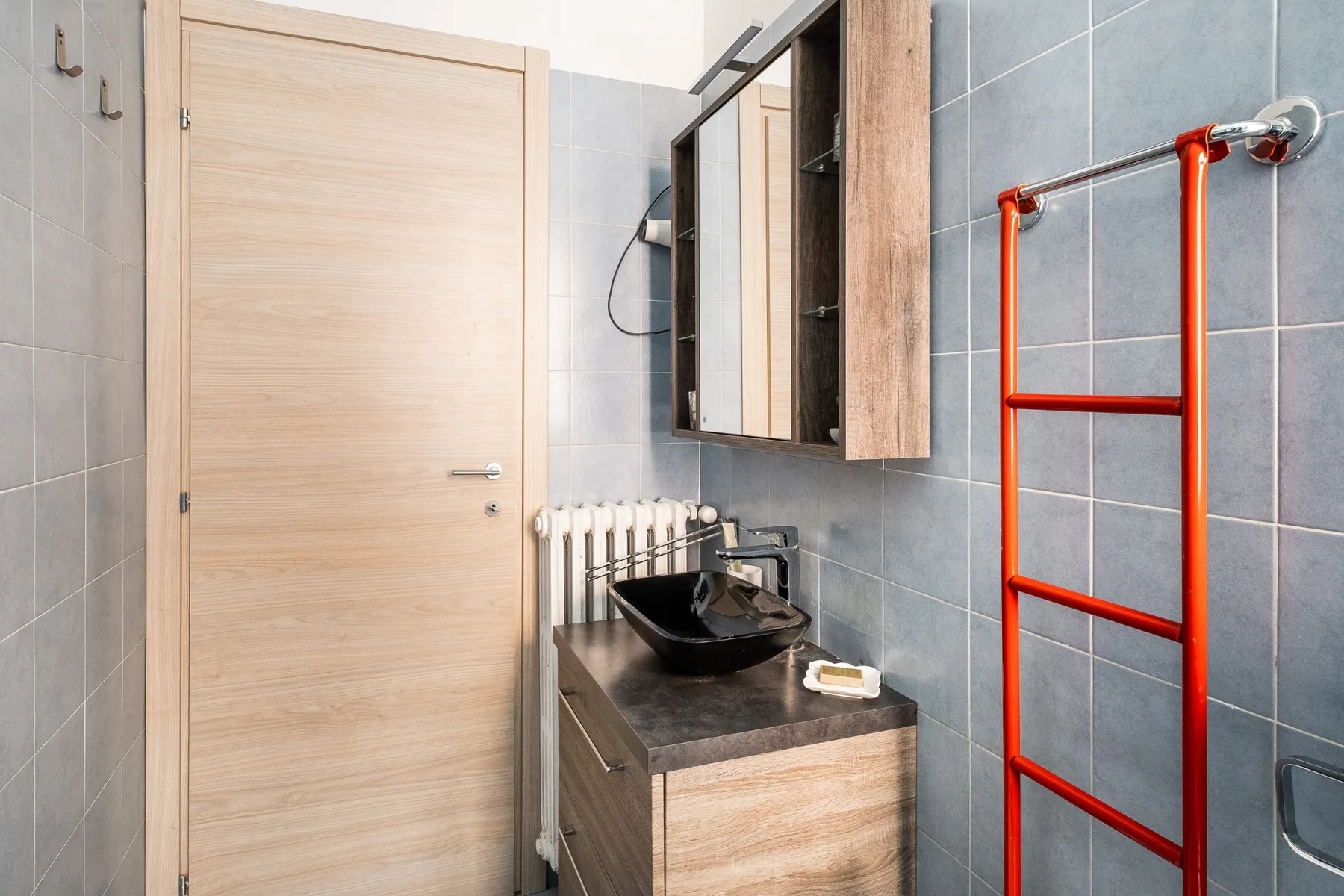 A tiled bathroom with a sink vanity and a bright red towel rail.