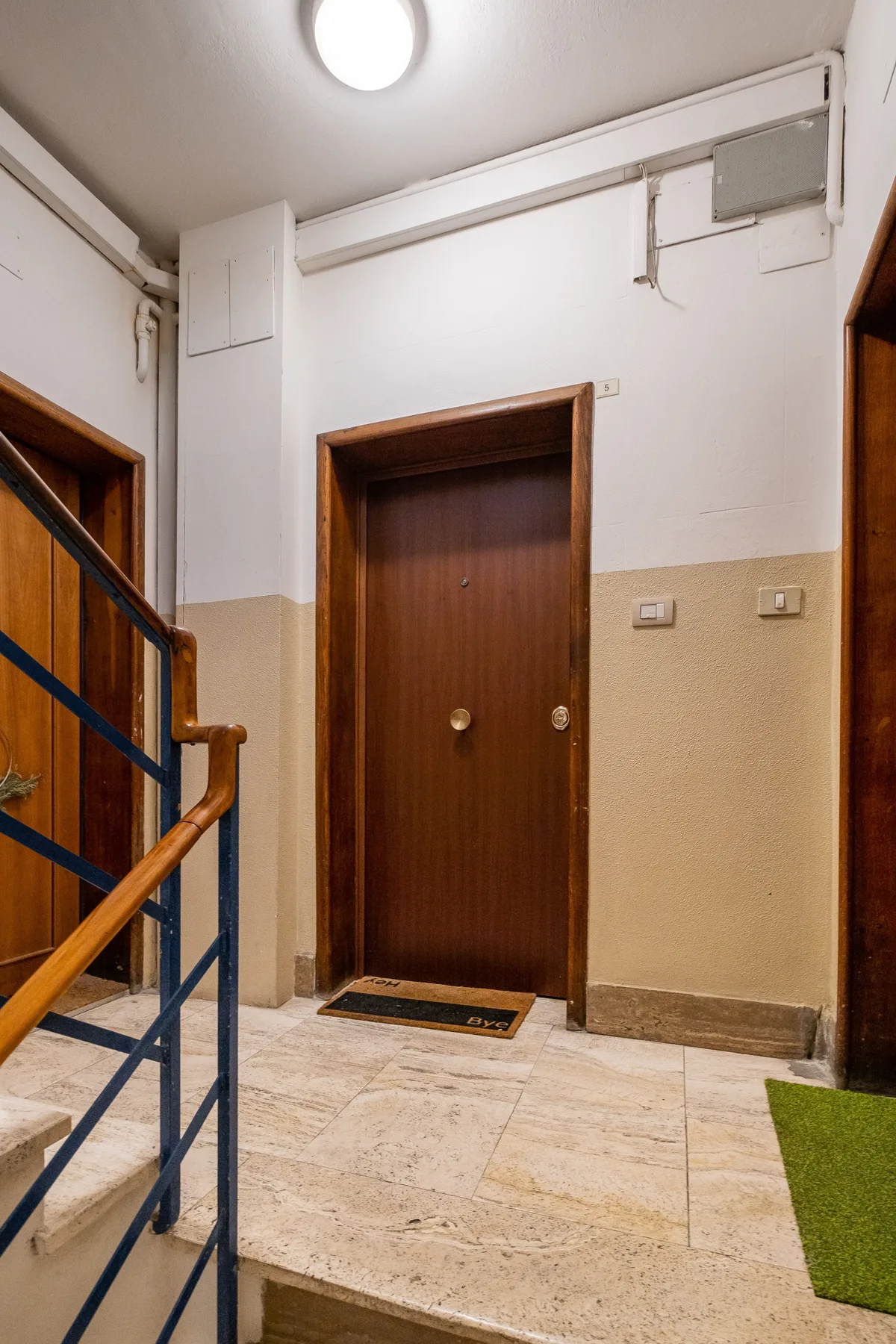 An indoor hallway landing with a brown door and staircase railing.