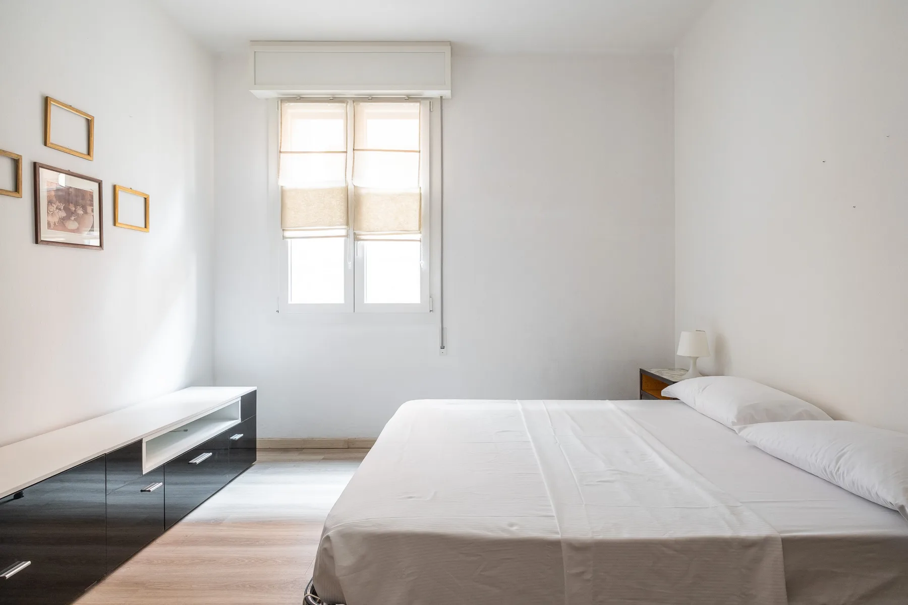 A bright bedroom with a bed, a window, and a low cabinet.