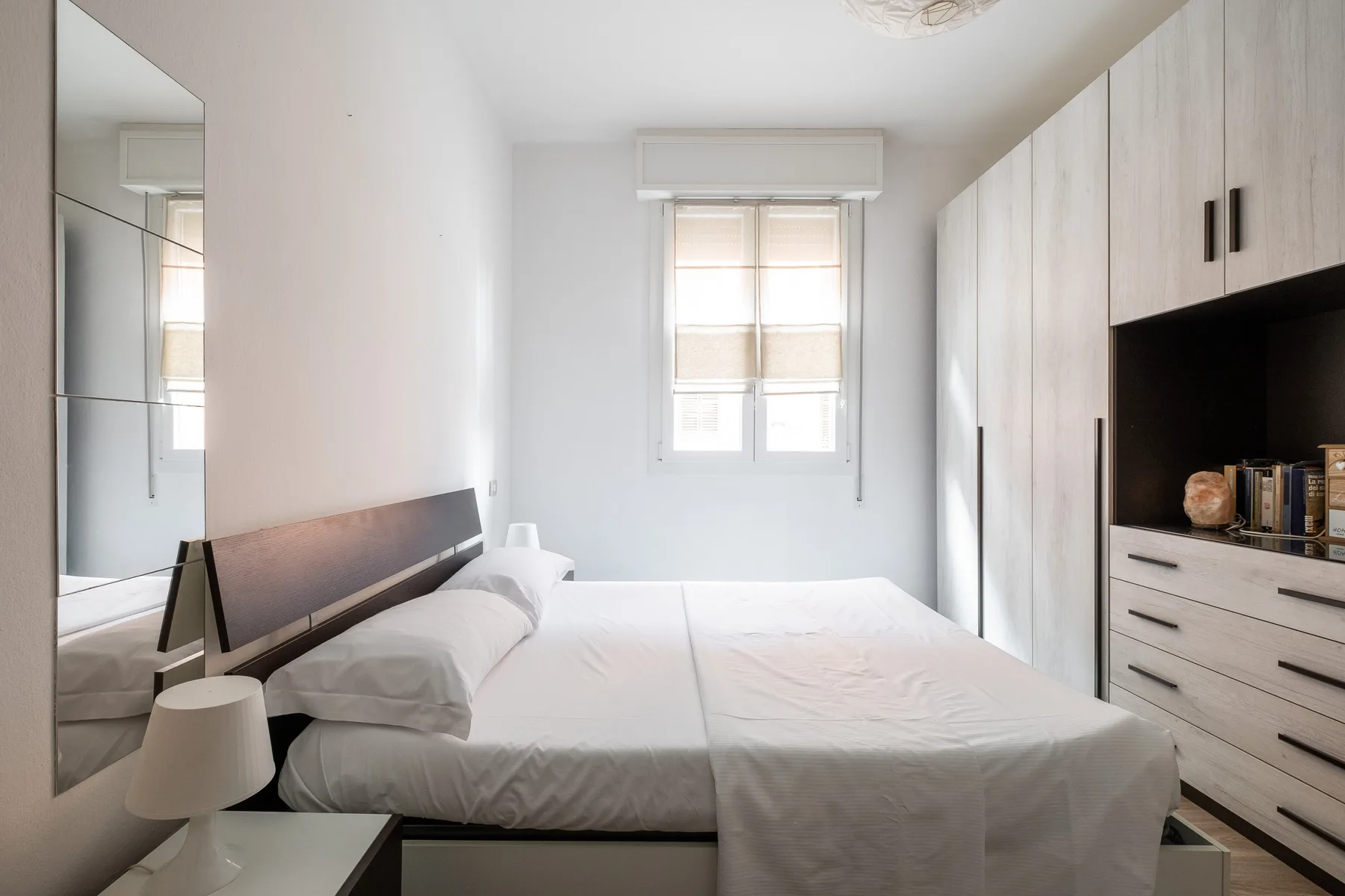 A bright bedroom with a bed, a window, and built-in cabinetry.