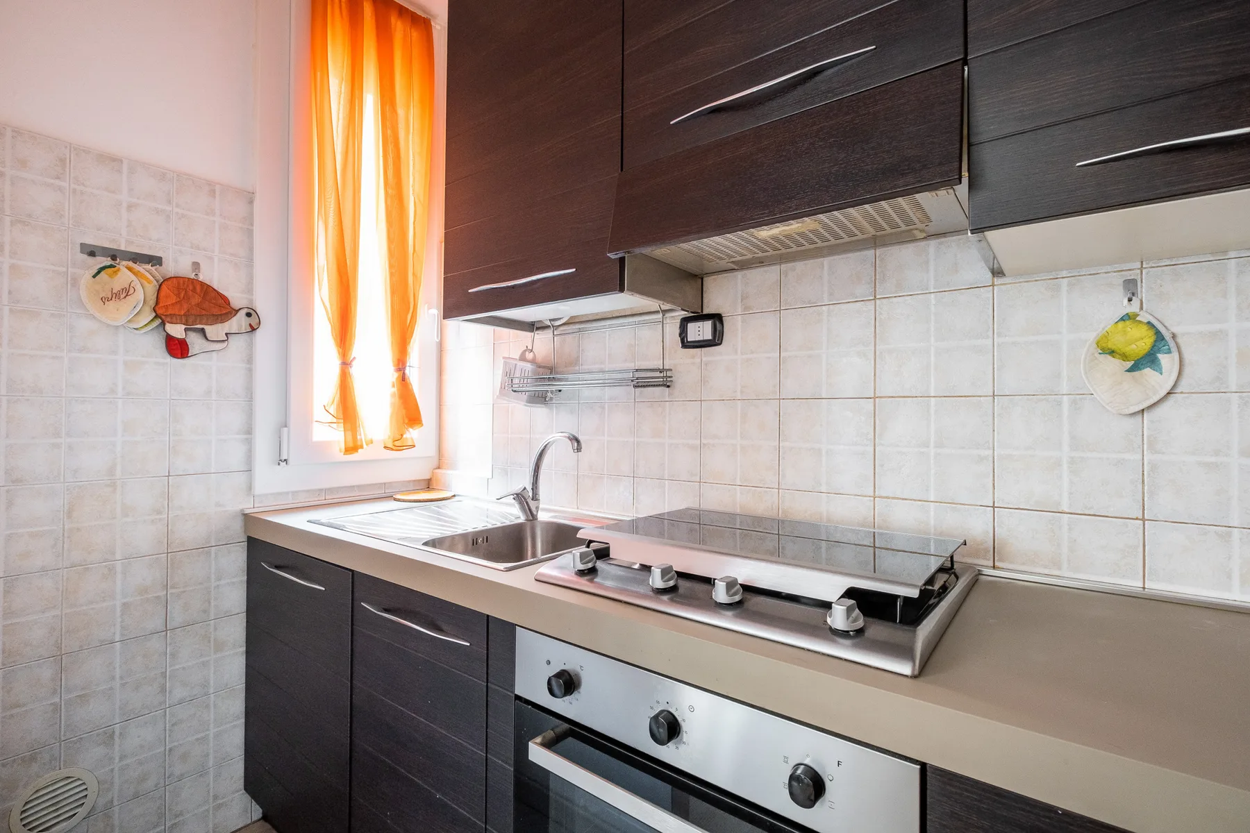 A tiled kitchen with dark cabinets, a countertop stove, and a sink.