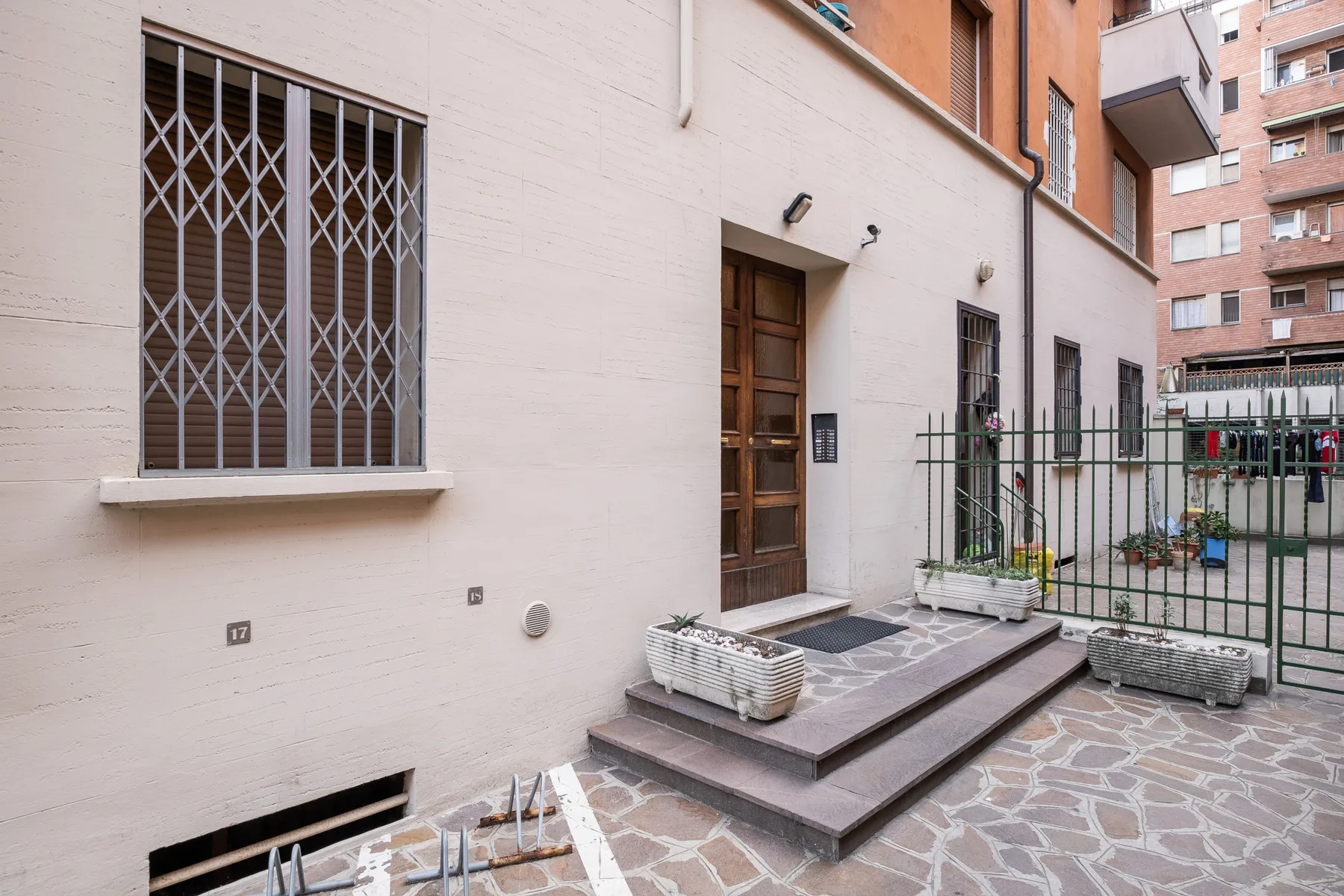 A building entrance opens onto a paved courtyard with barred windows and planters.