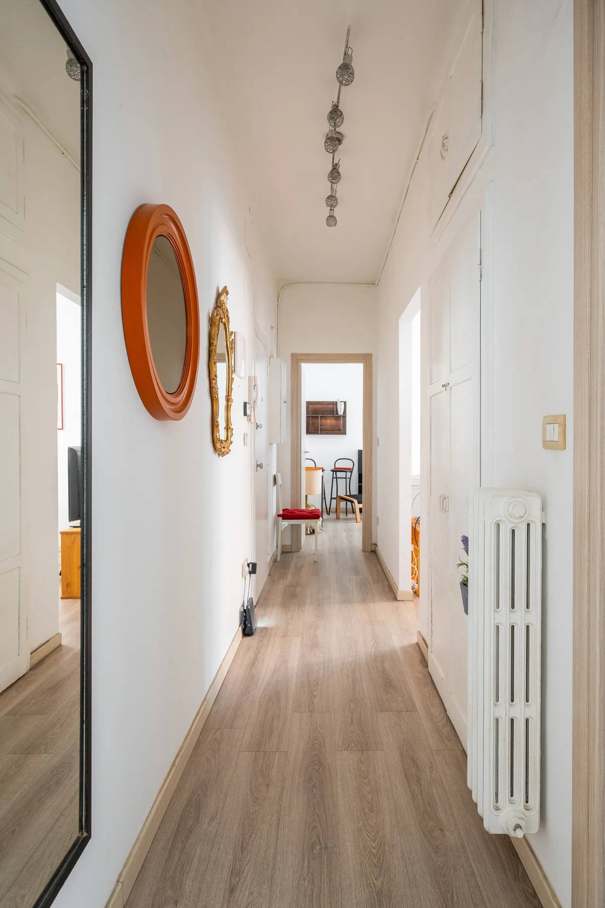 A bright hallway with light wood flooring and decorative mirrors along the wall.