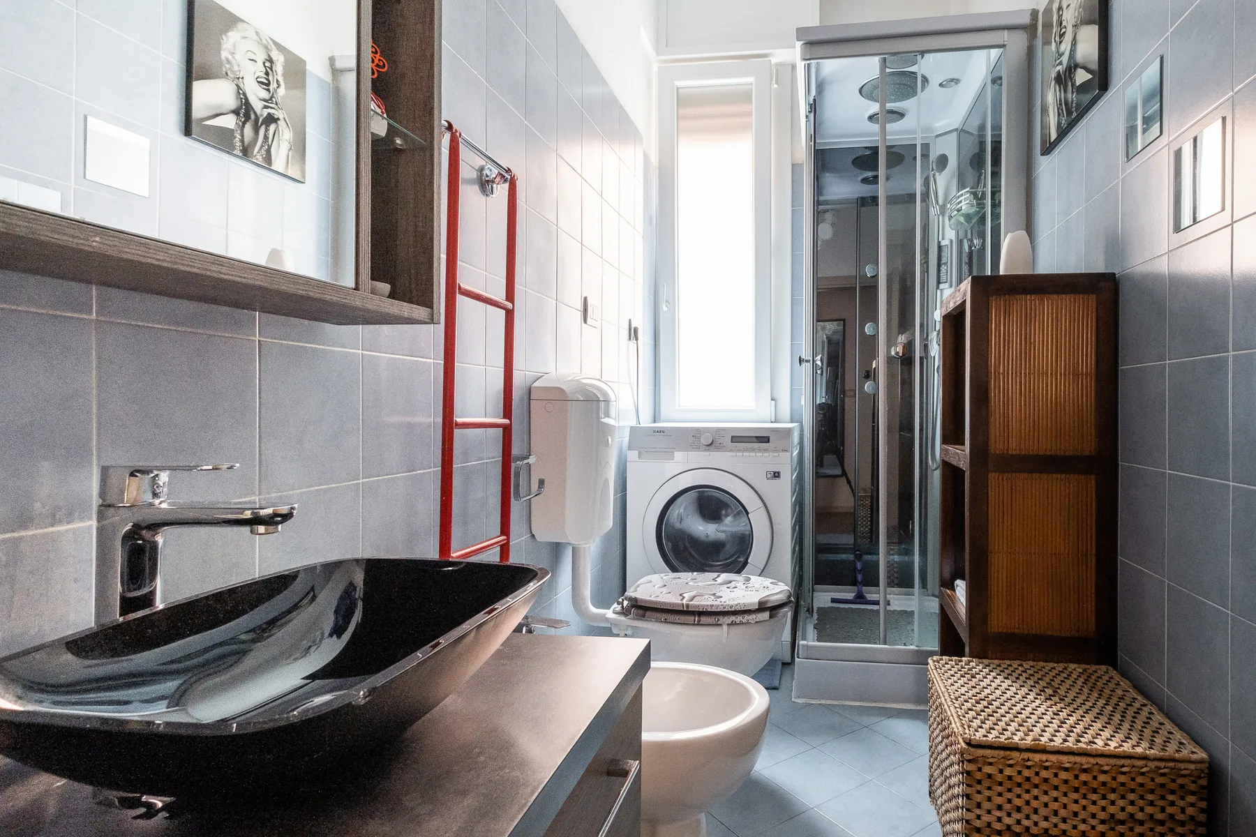 A tiled bathroom with a sink, washing machine, and glass shower.