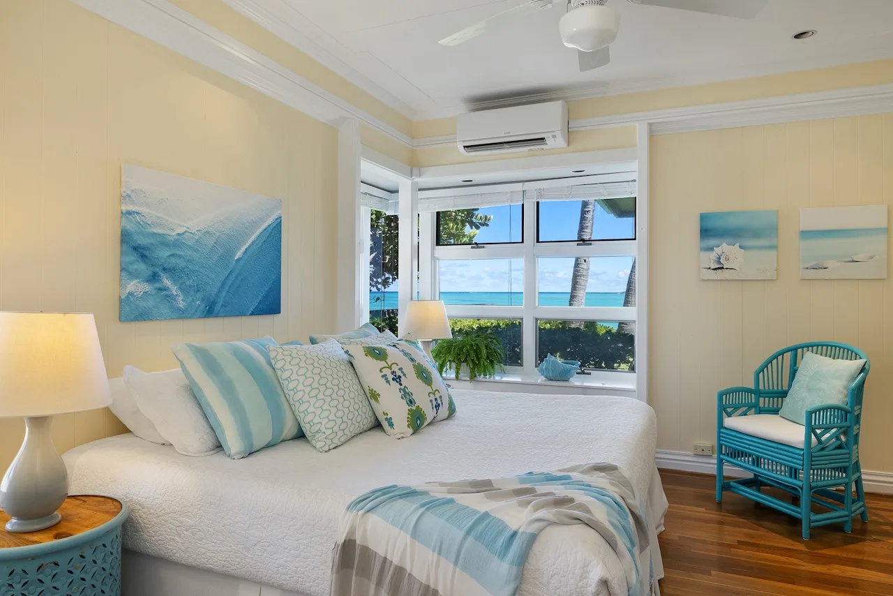 A bright bedroom with a bed facing large windows overlooking the water.