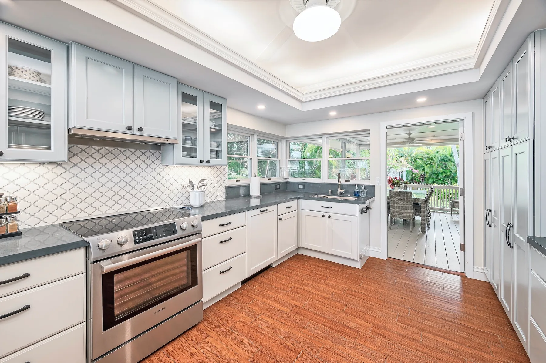 A bright kitchen with white cabinetry, dark counters, and a dining area by the windows.