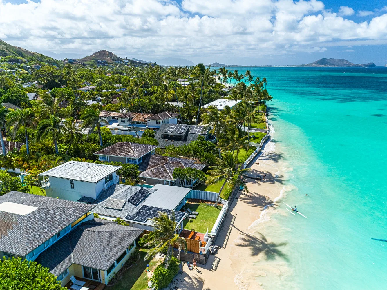 Aerial coastal scene with homes along a sandy beach and turquoise water.
