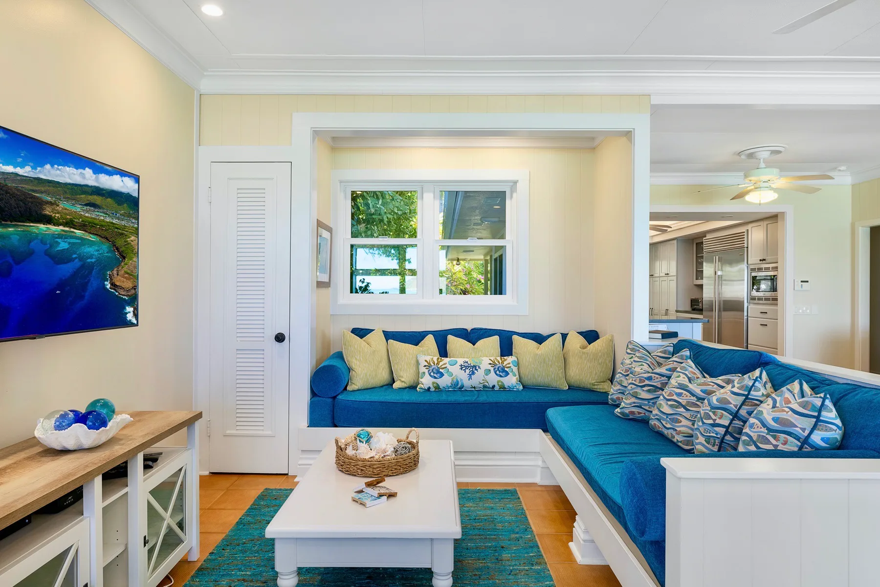 A bright living room with blue seating, a coffee table, and a television.