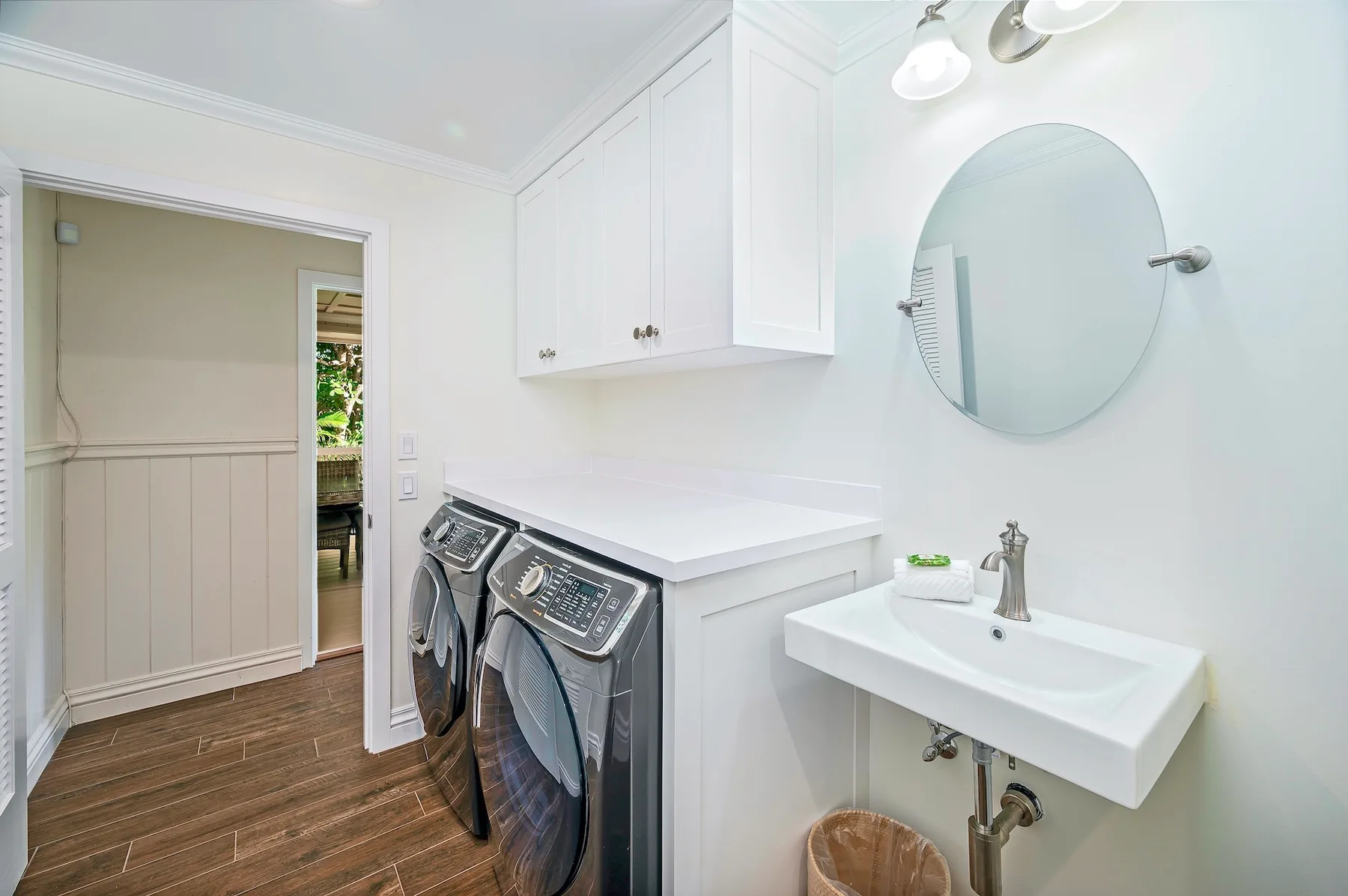 A laundry room with a washer and dryer beside a sink and round mirror.