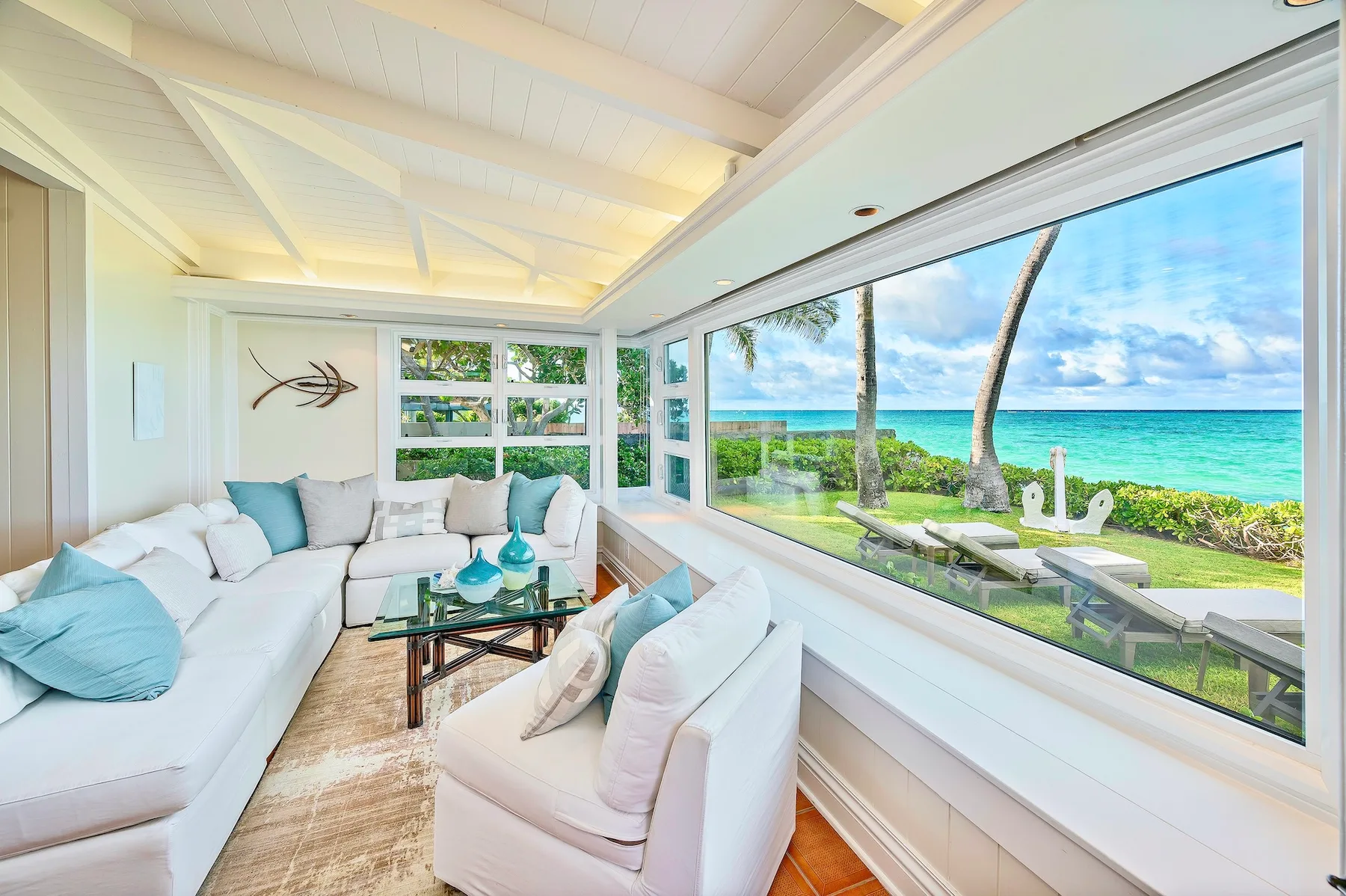 A bright living room with seating beside large windows overlooking the ocean.