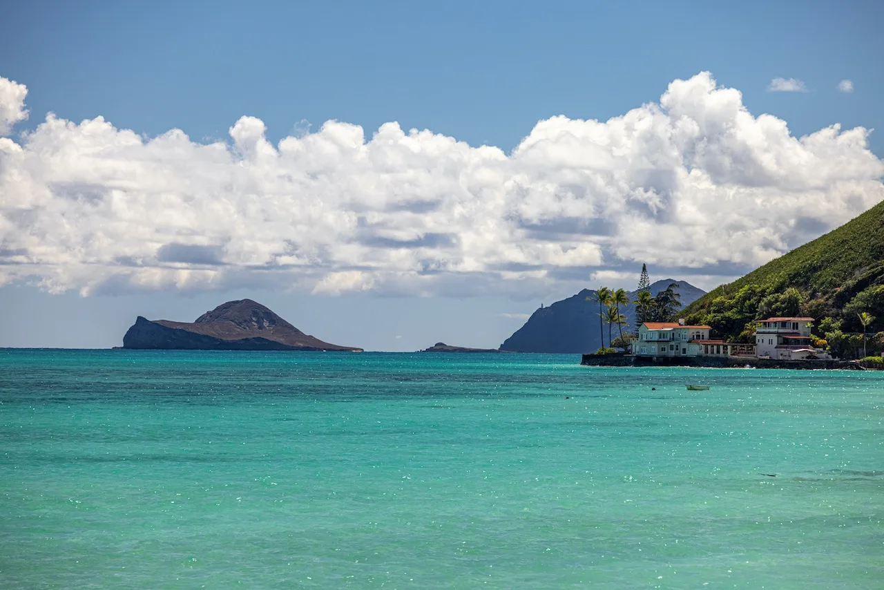 A coastal bay with turquoise water, distant islands, and hillside buildings.