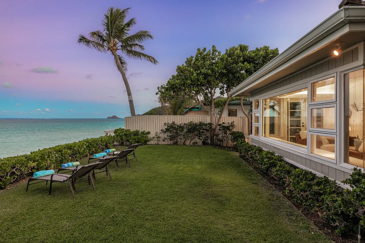 A grassy beachfront yard beside a house, with lounge seating overlooking the water.
