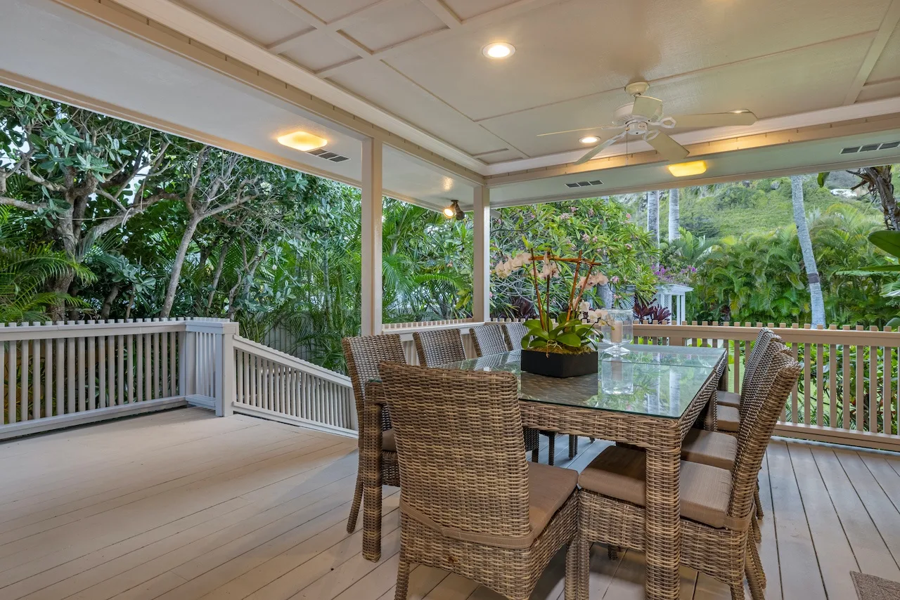A covered outdoor dining area with wicker seating and views of tropical greenery.