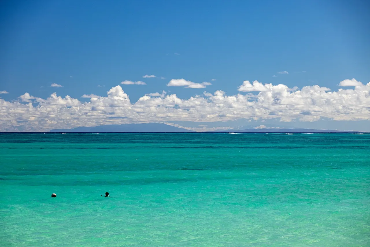 A tropical seascape with turquoise water, distant islands, and a cloudy blue sky.