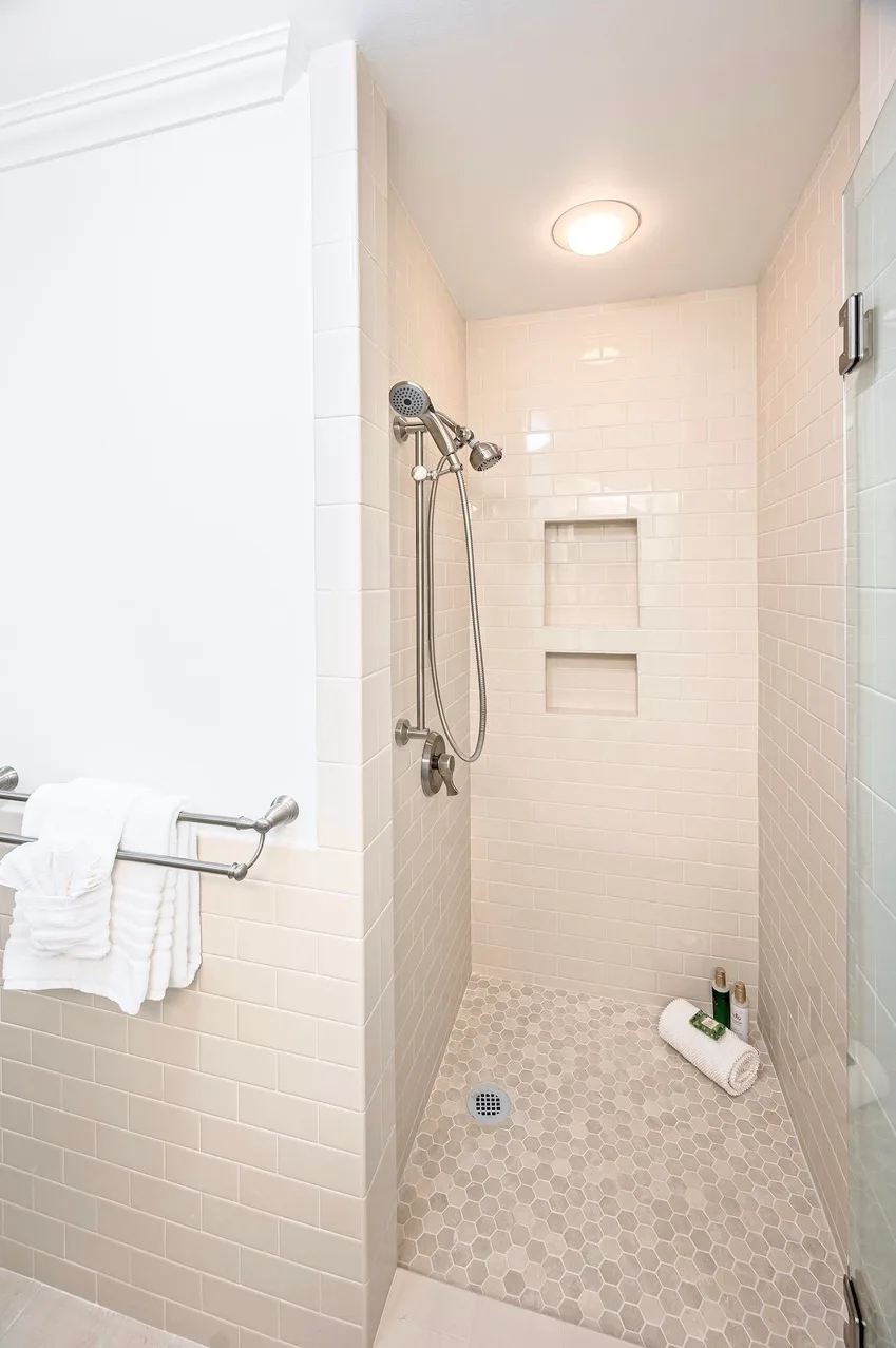 A tiled bathroom with a walk-in shower, recessed wall shelves, and towels on a rack.