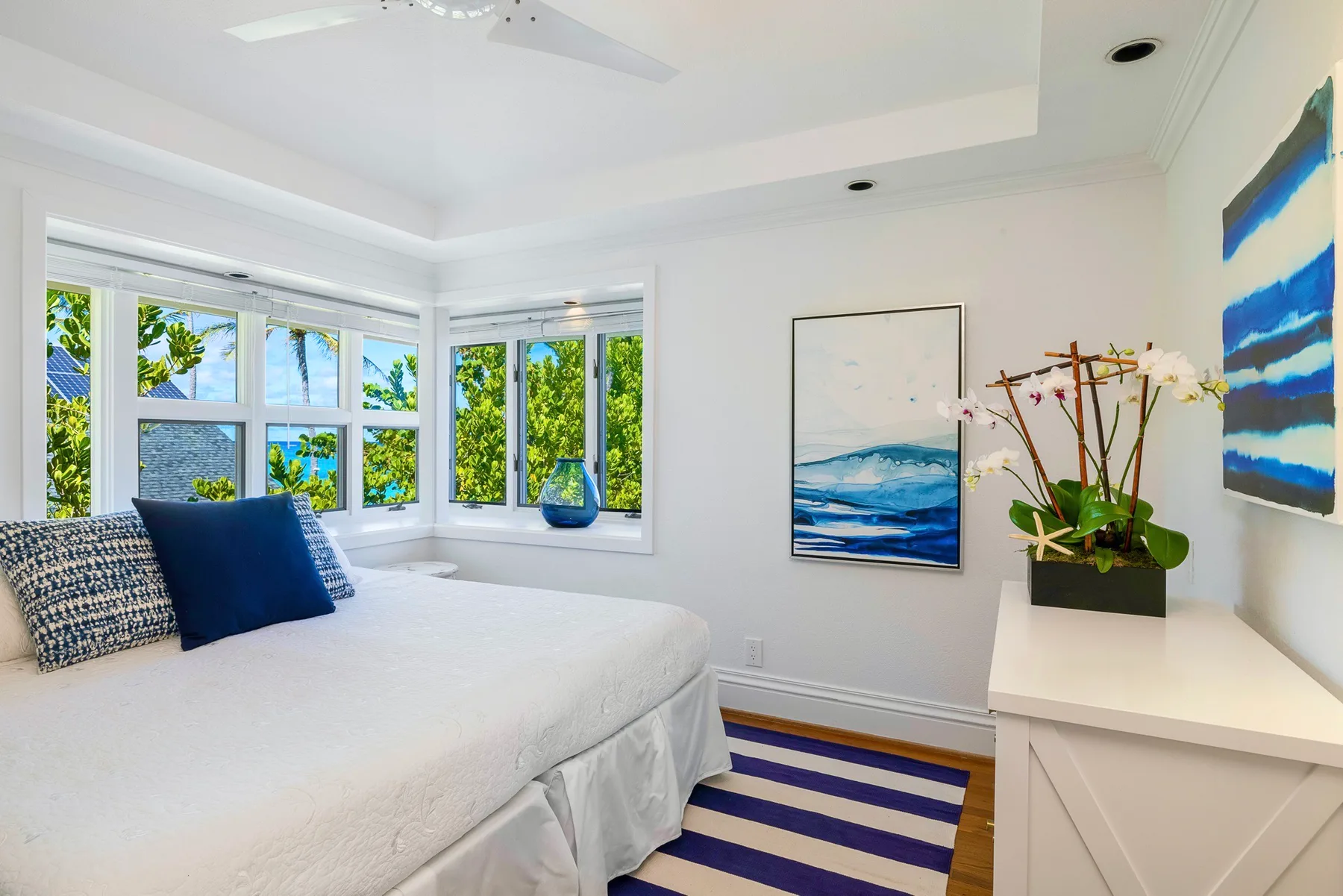 A bright bedroom with a white bed, large windows, and blue accents.