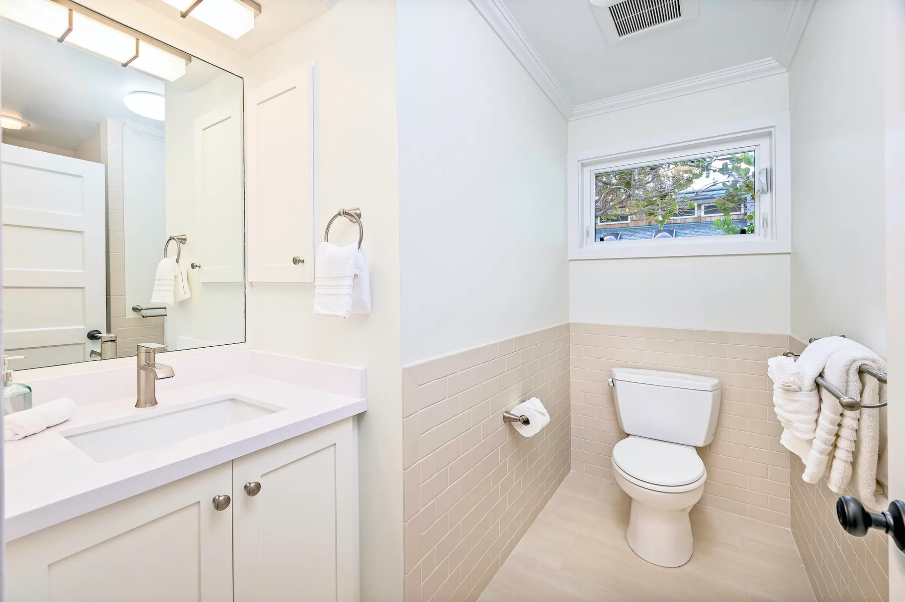 A bright bathroom with a toilet, sink, and window.