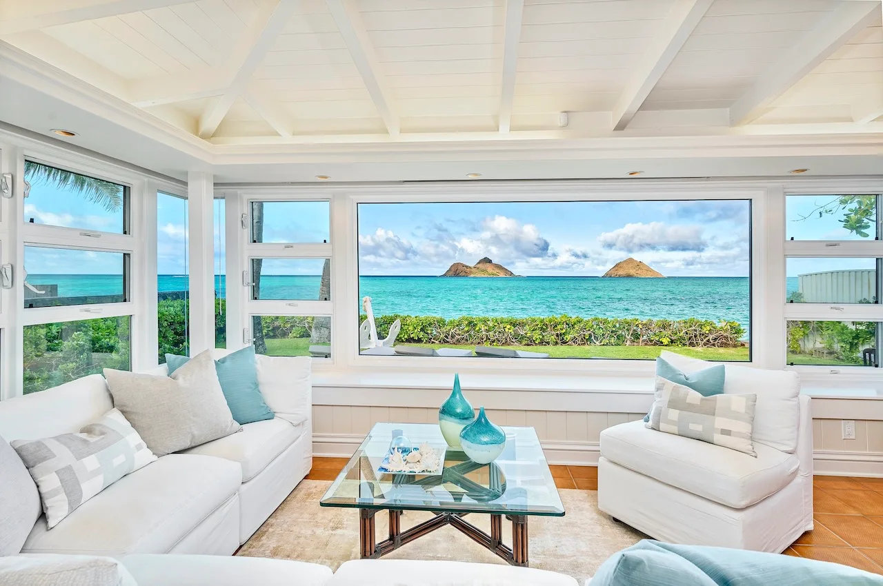 A bright living room with white seating and a wide ocean view through the windows.