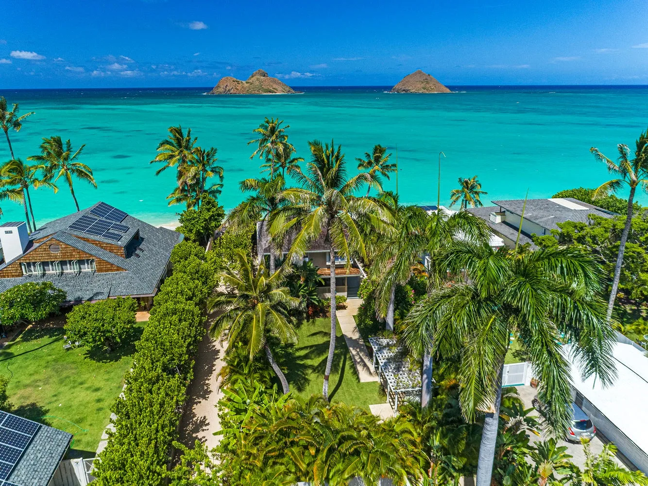 Aerial view of palm-lined homes beside a turquoise ocean and two offshore islets.