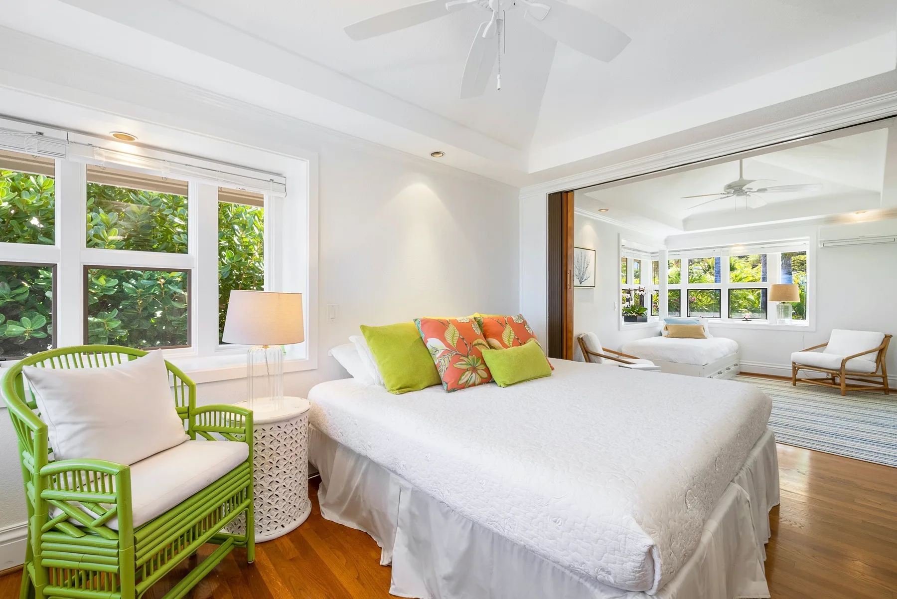 A bright bedroom with a large bed and green seating beside broad windows.
