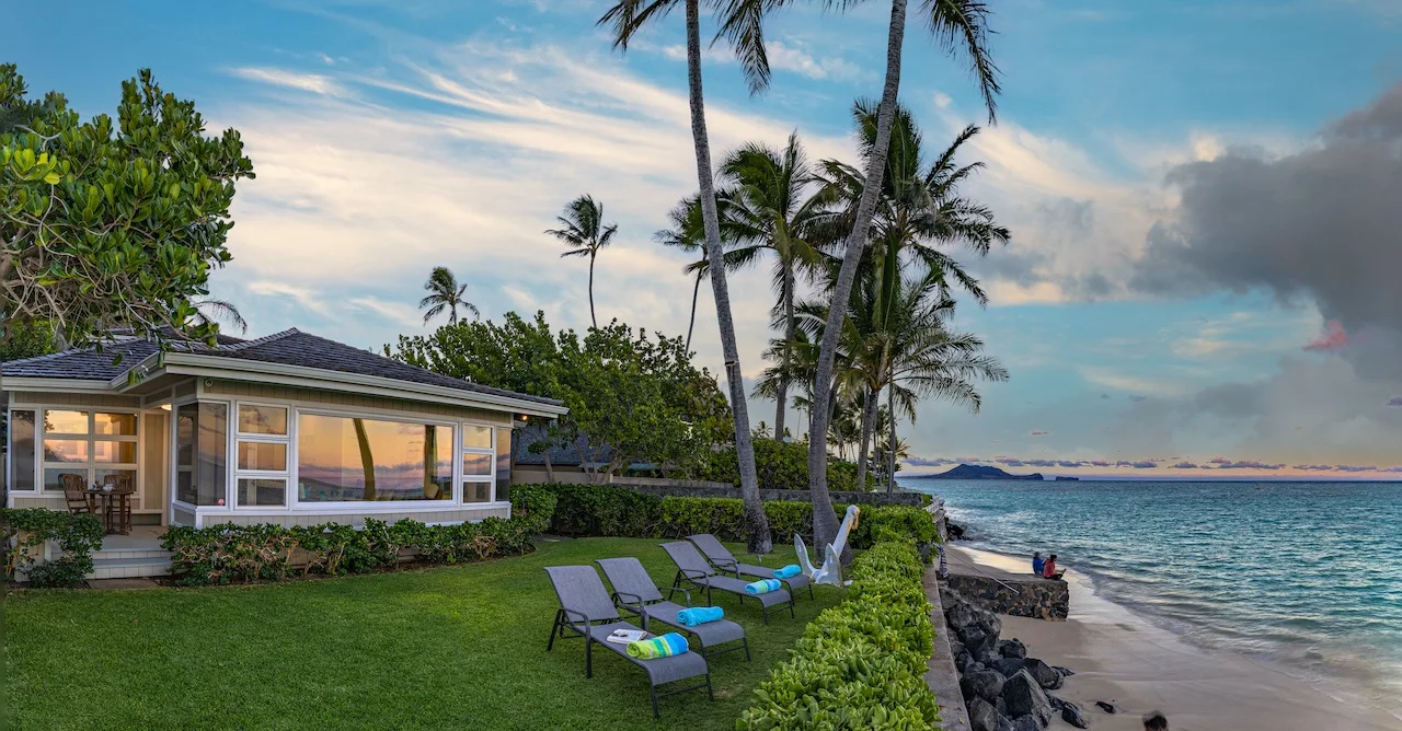 A beachfront lawn with outdoor seating beside a low house and the ocean.