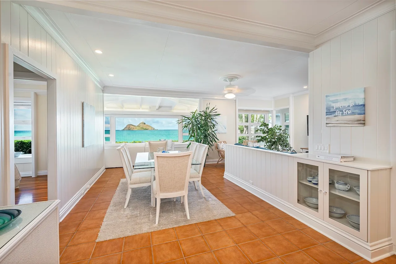 A bright dining area opens toward ocean views, with a table and chairs on a rug.