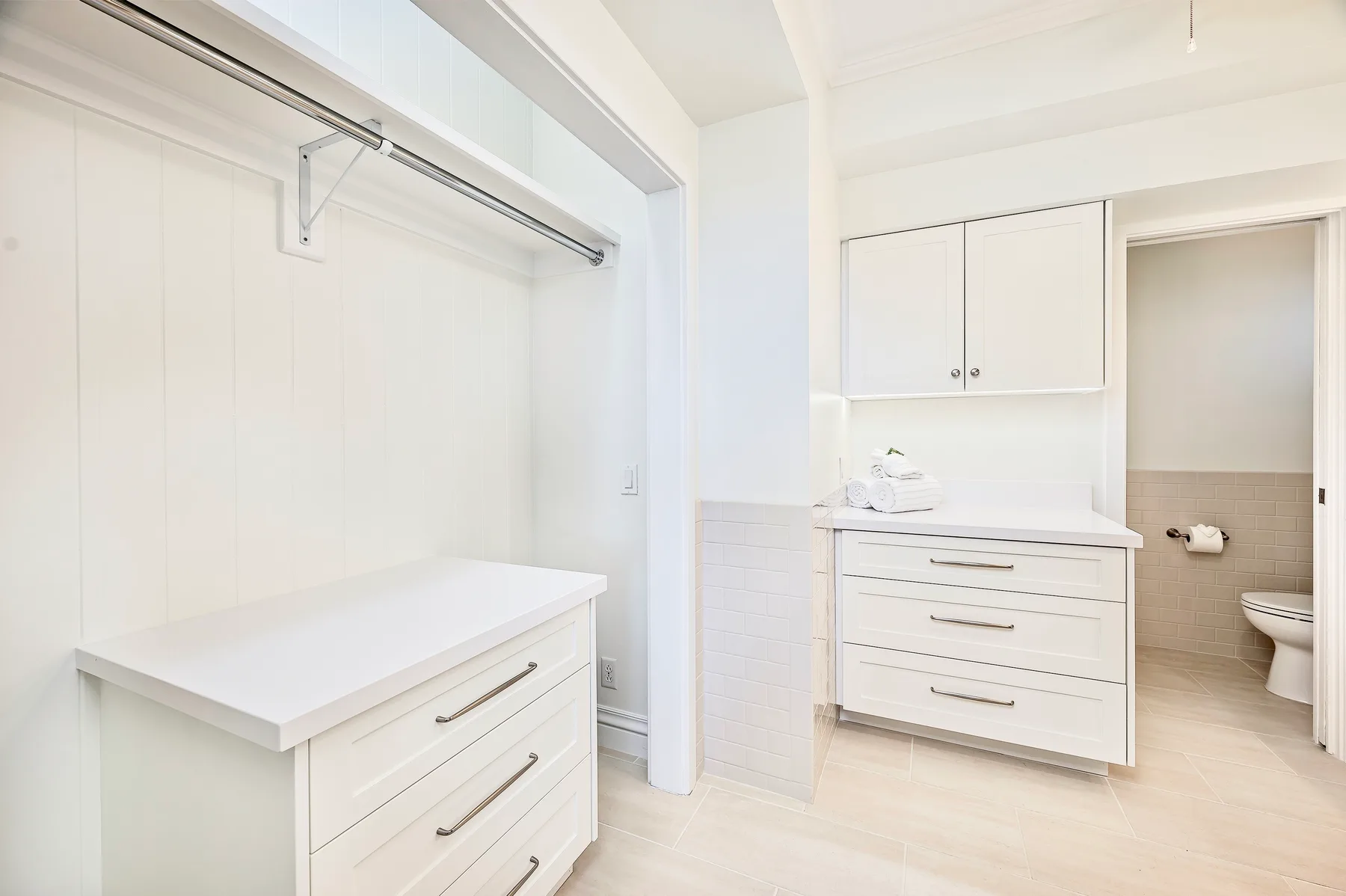 A bright bathroom with white cabinetry and an open doorway to the toilet area.