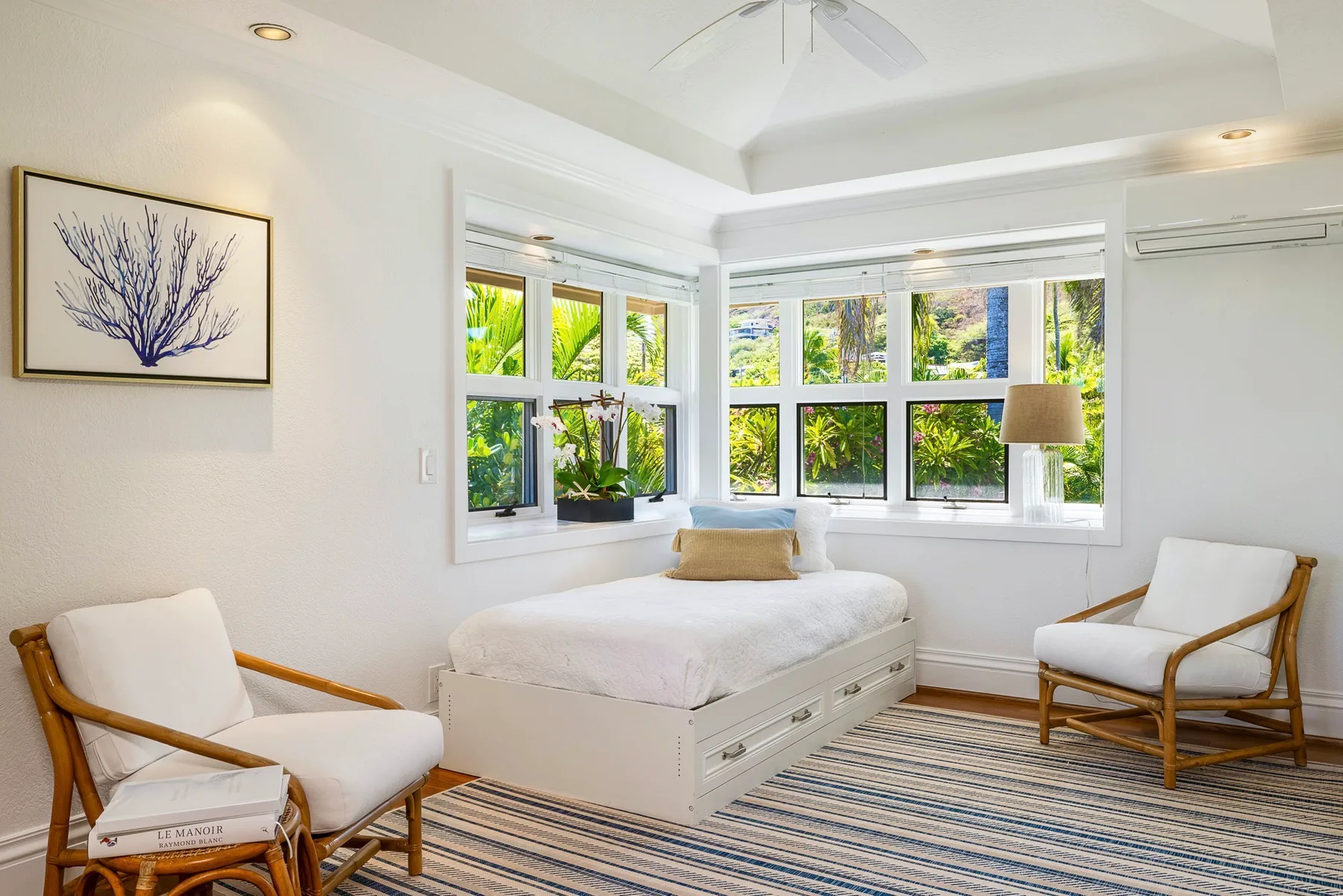 A bright bedroom with a bed, seating, and large windows overlooking greenery.