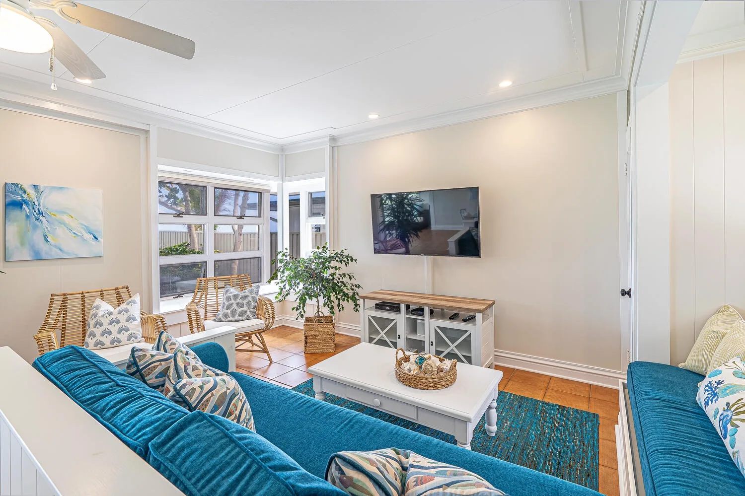 A bright living room with blue seating, a coffee table, and a wall-mounted television.
