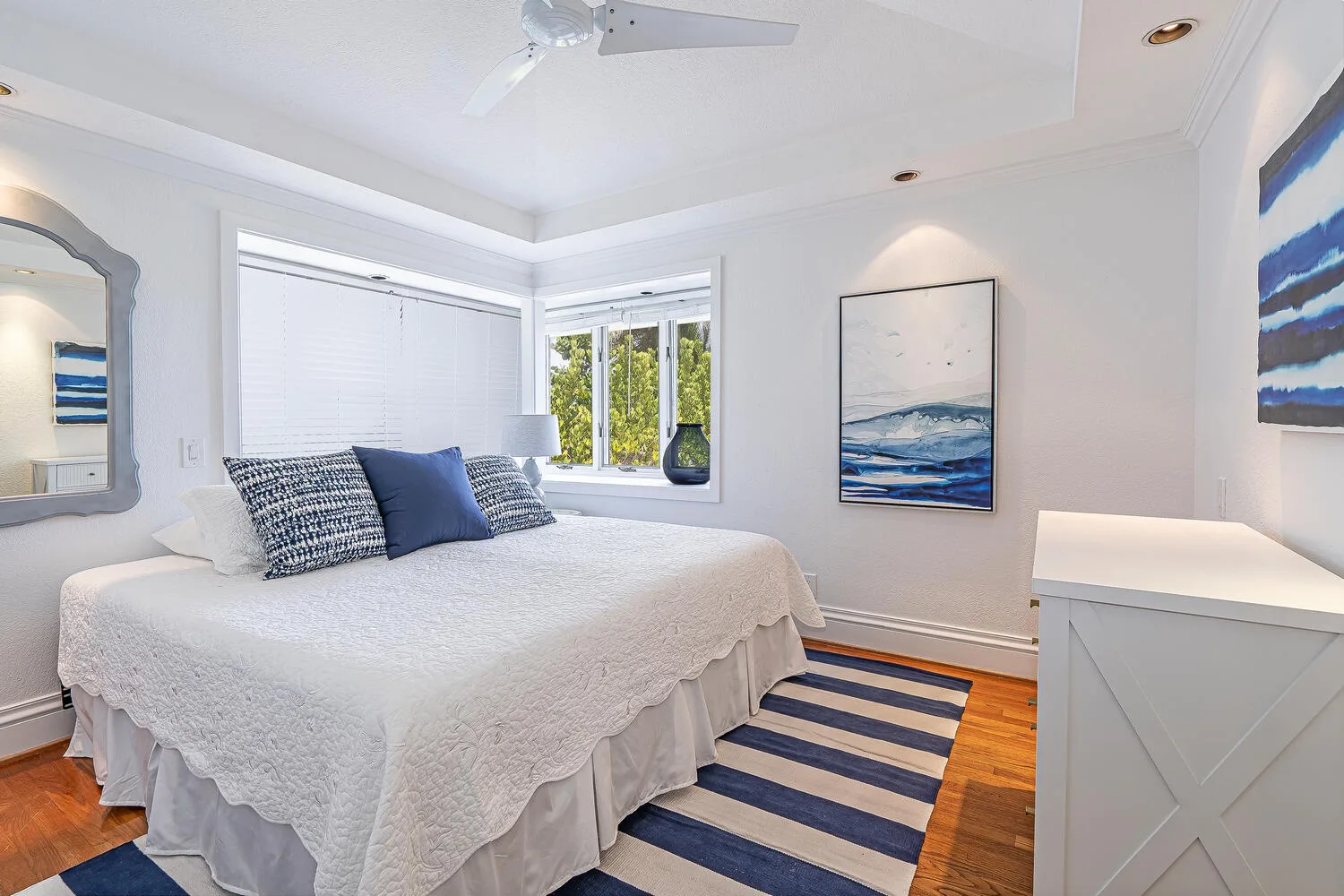 A bright bedroom with a neatly made bed and ocean-themed artwork.