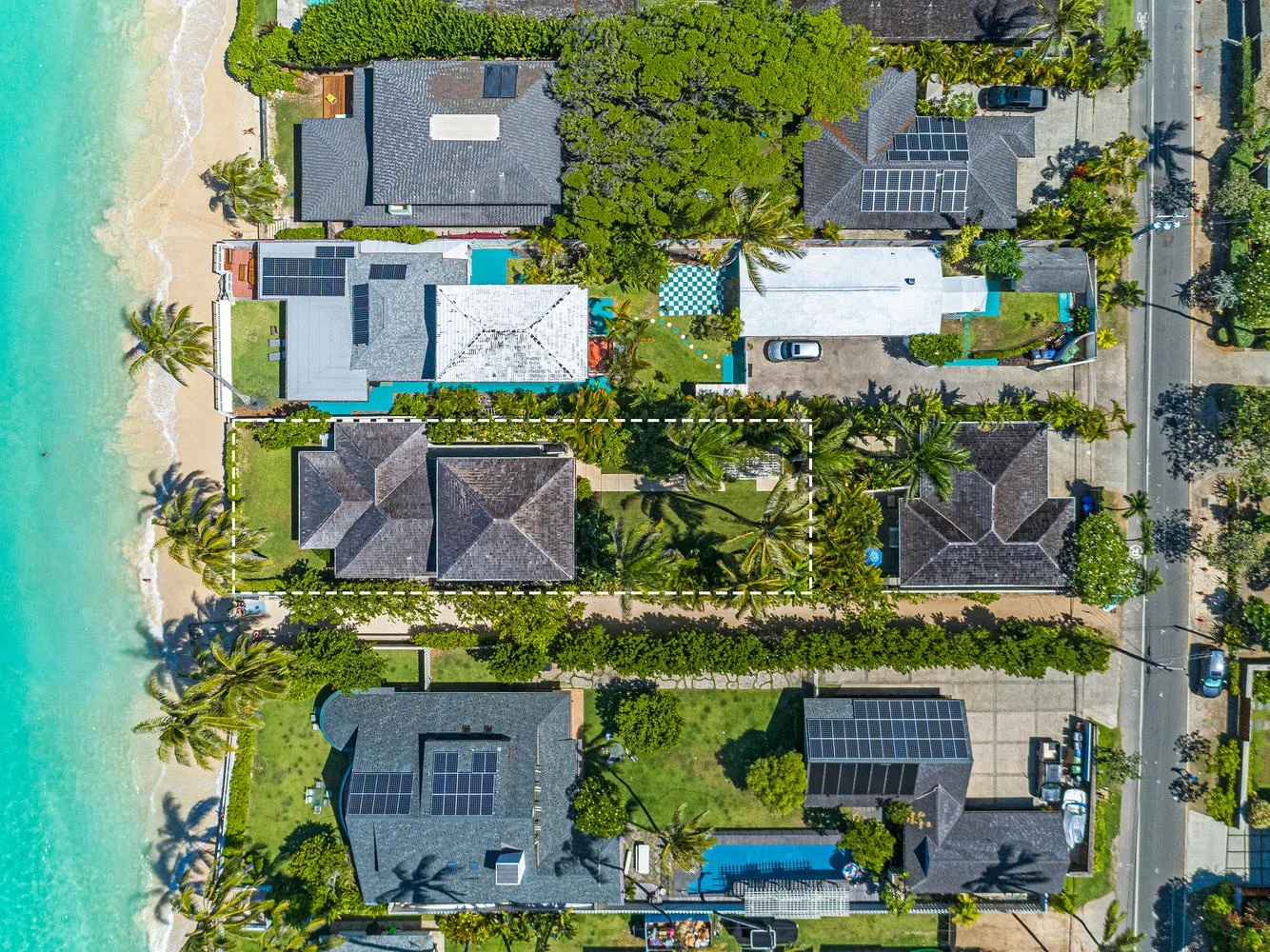 Aerial view of beachfront buildings surrounded by greenery beside turquoise water.