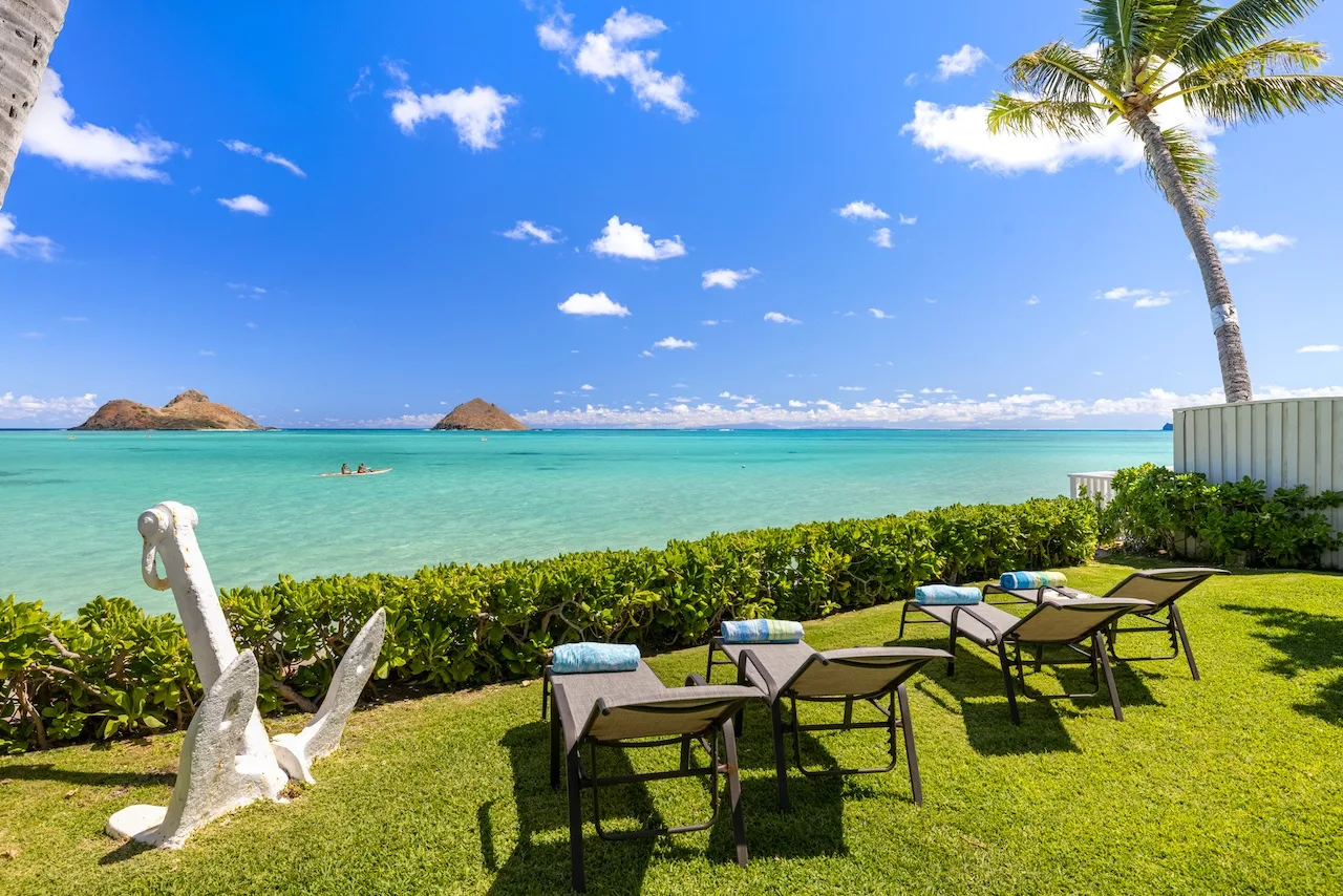 A seaside lawn with lounge seating overlooks turquoise water and distant islands.