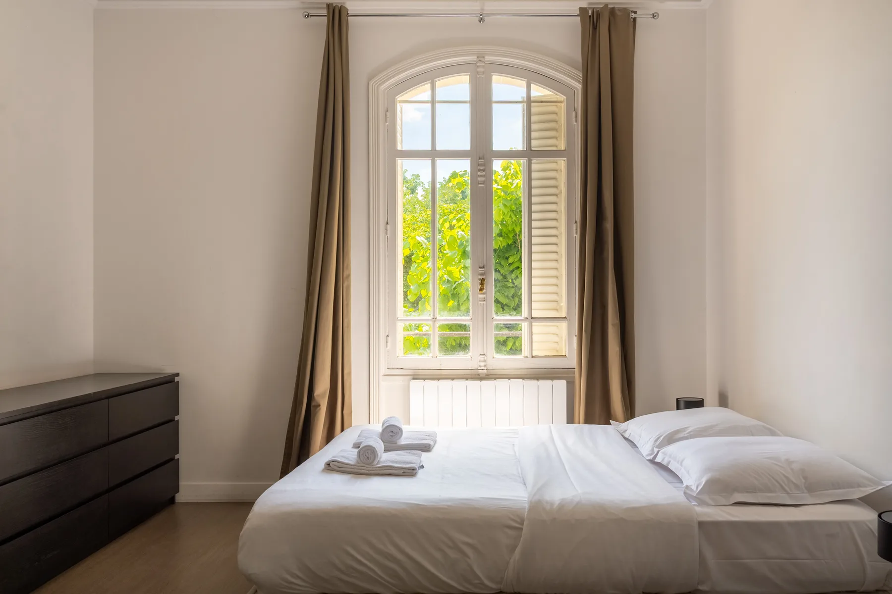 Un dormitorio con una cama bien tendida bajo una ventana grande.