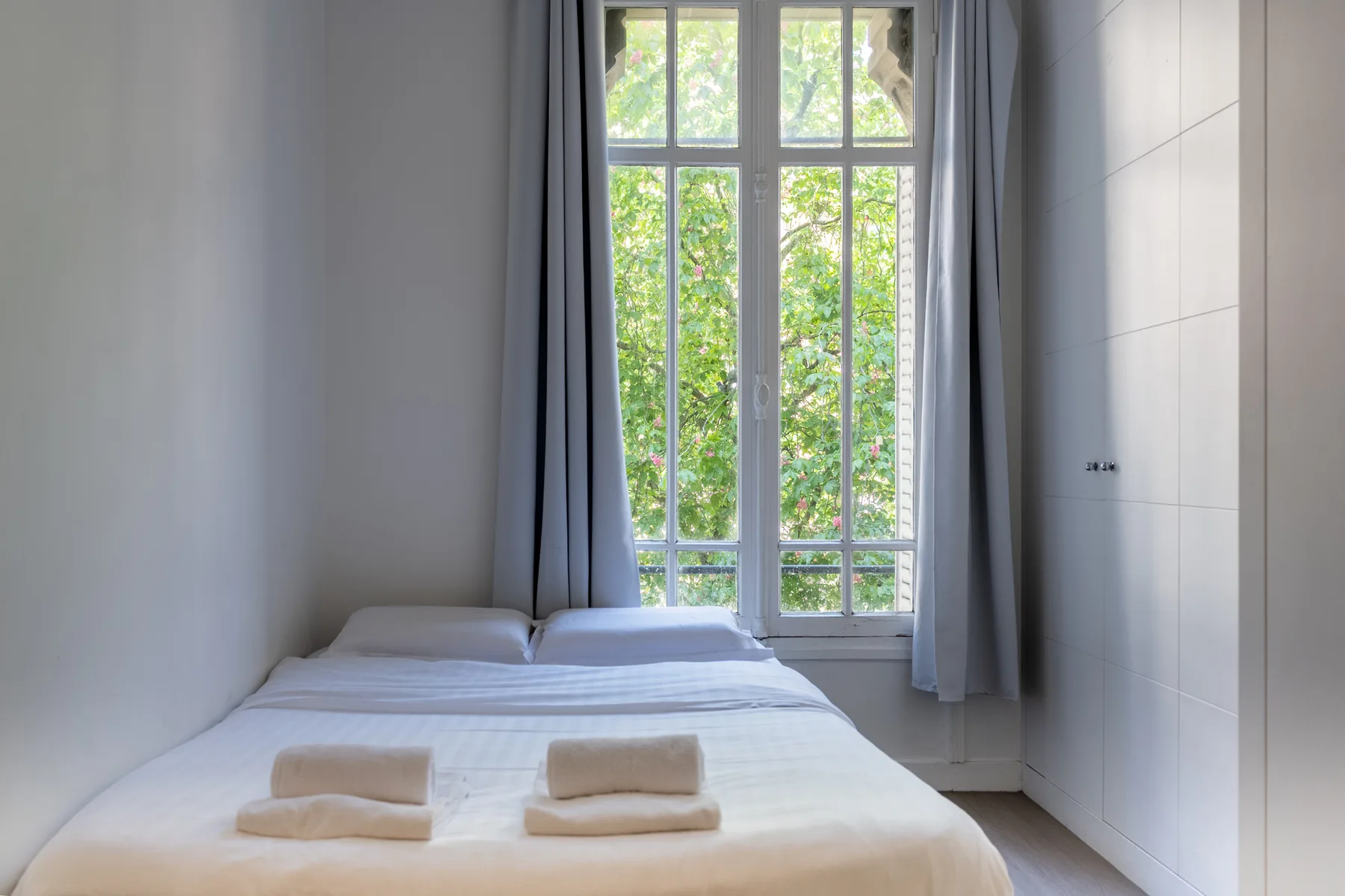 Un dormitorio con una cama bien tendida junto a una ventana alta.