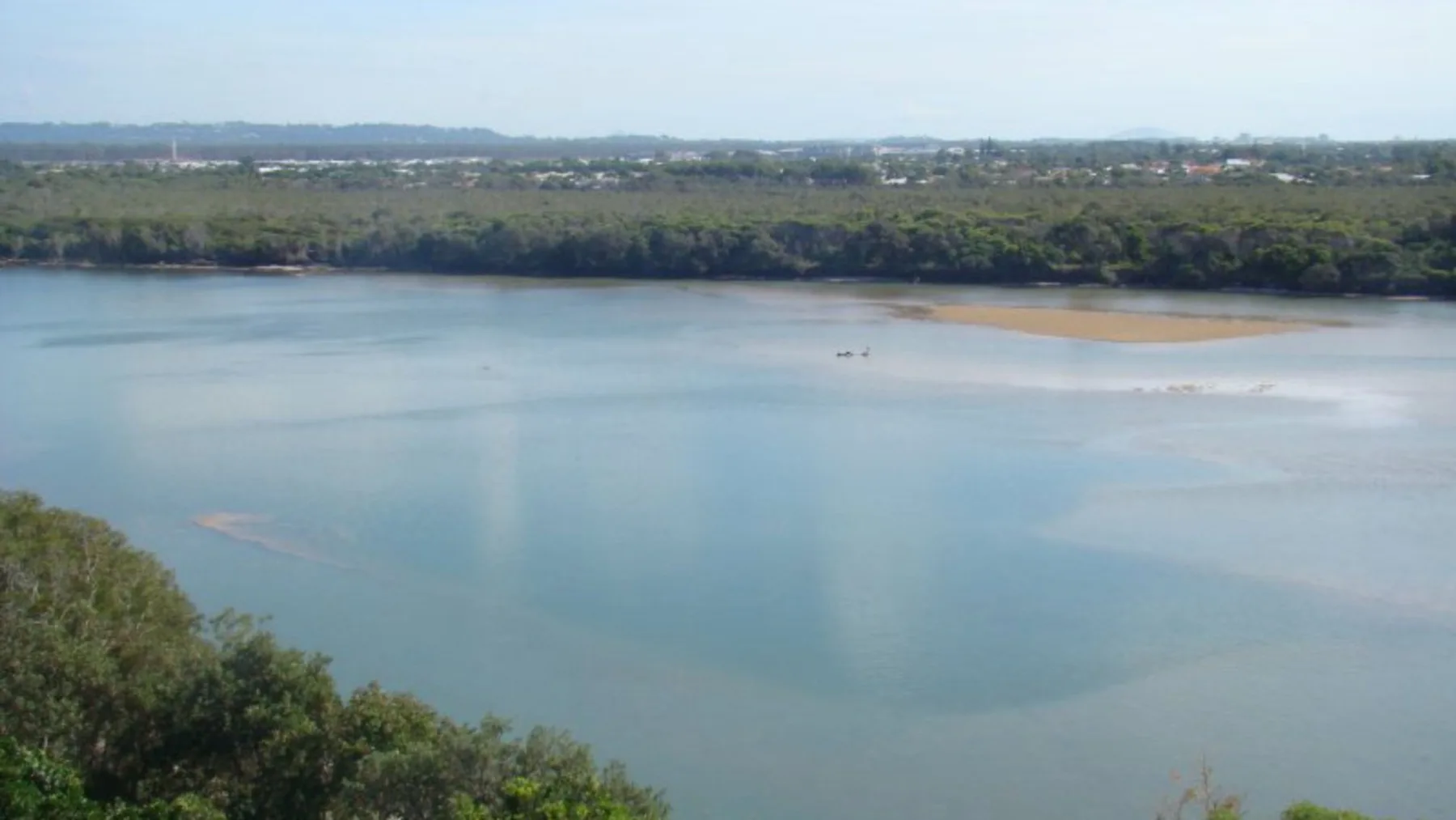 Un amplio lago se extiende hacia una orilla boscosa bajo un cielo despejado.