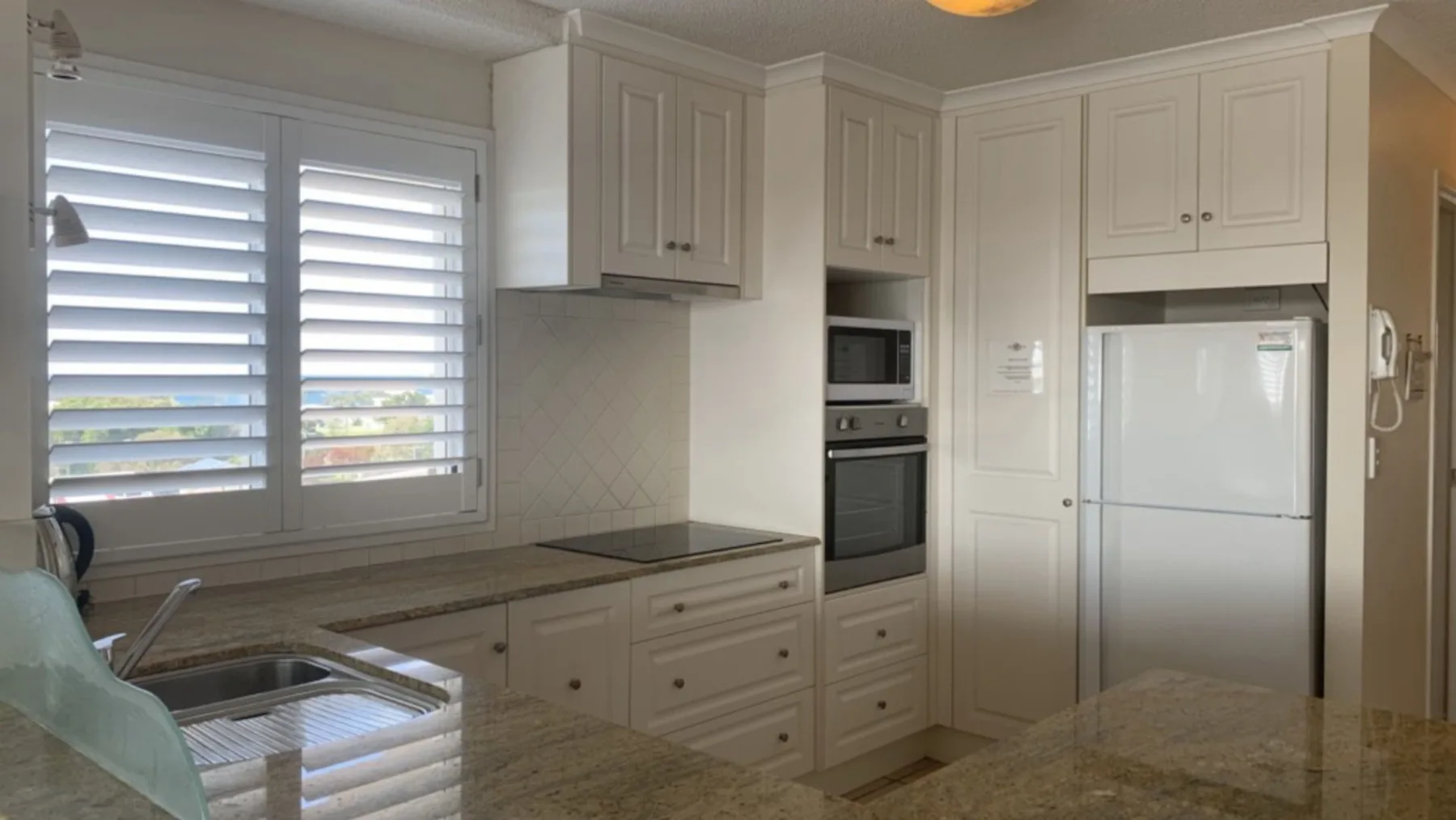 Una cocina luminosa con gabinetes blancos, un refrigerador y una ventana amplia.
