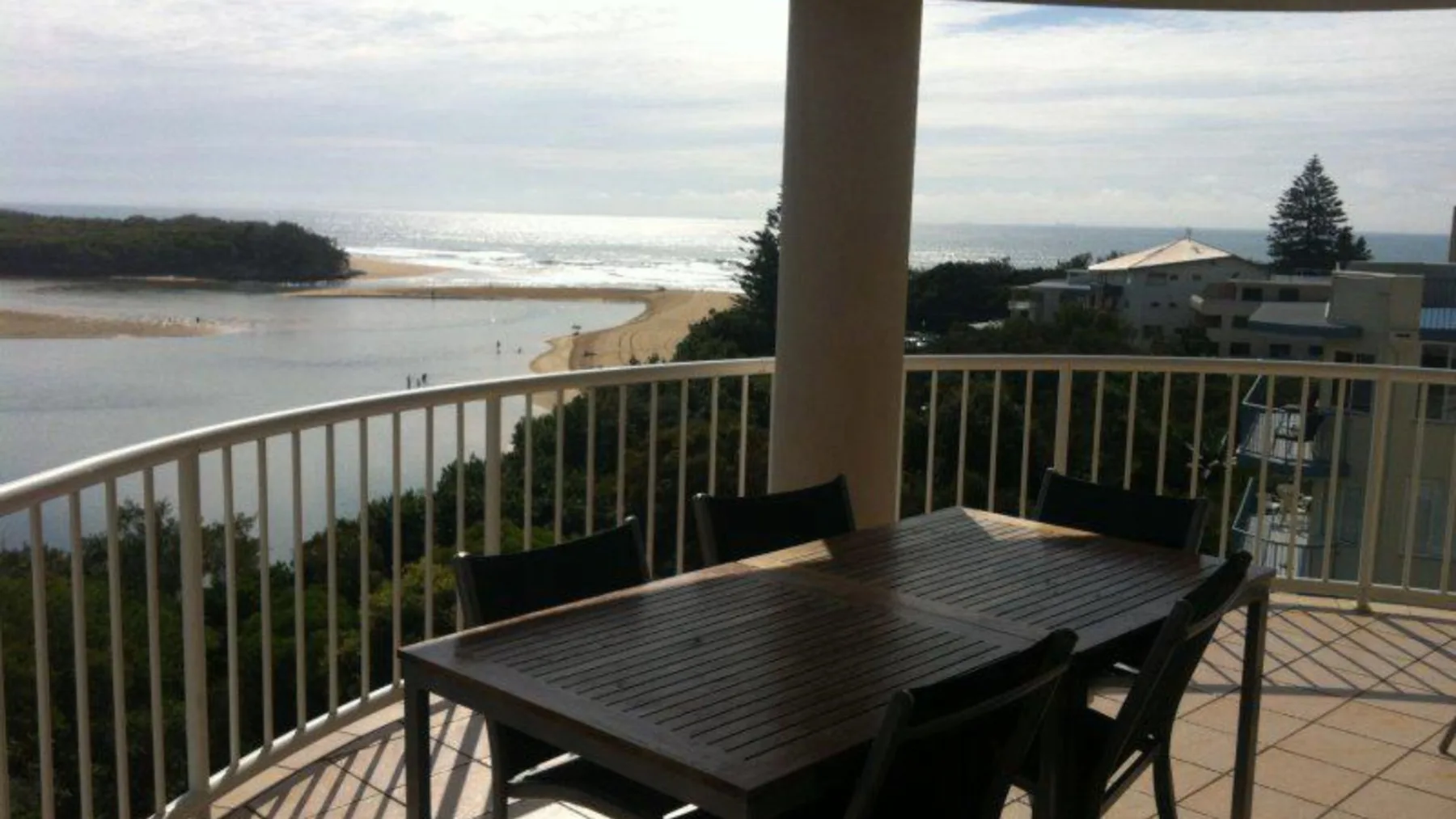 Una zona de comedor en un balcón mira a una laguna, una playa y el océano.