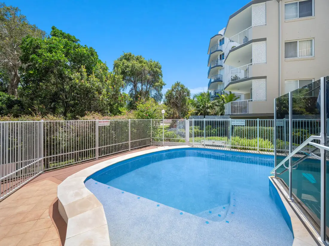 Una piscina al aire libre está junto a un patio cercado y un edificio de apartamentos.