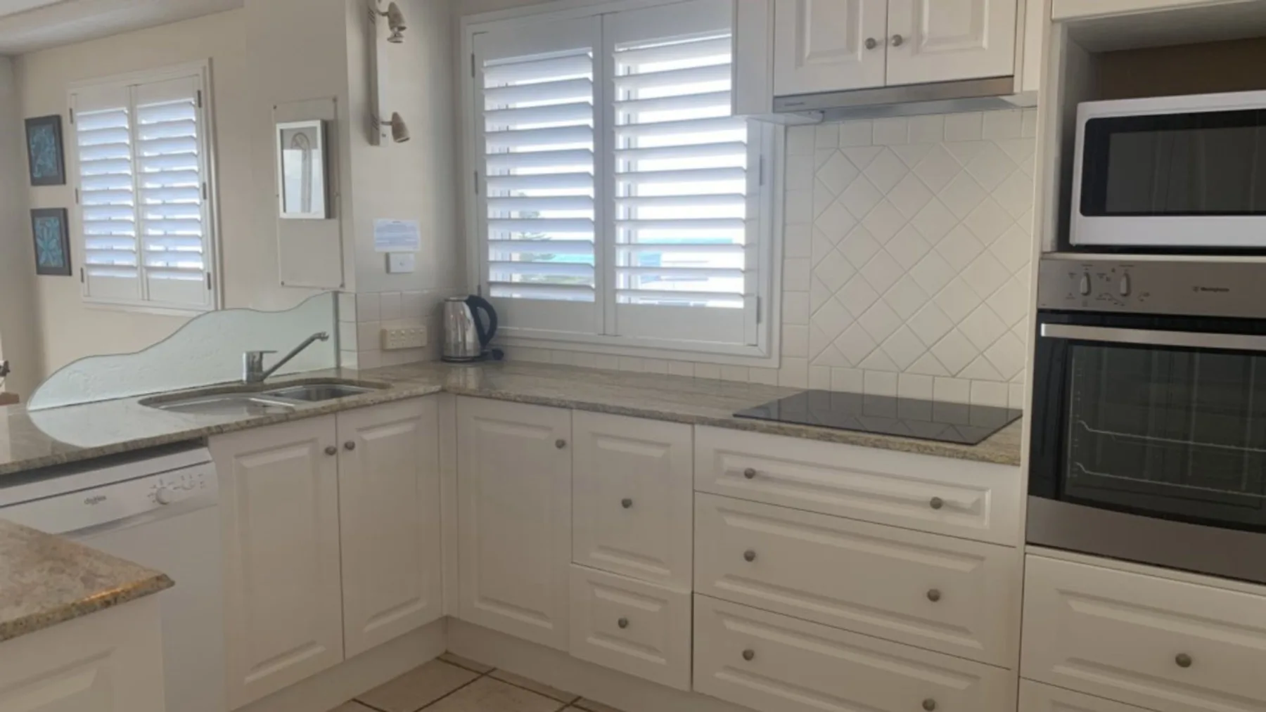 Una cocina luminosa con gabinetes blancos, encimeras y ventanas con persianas.