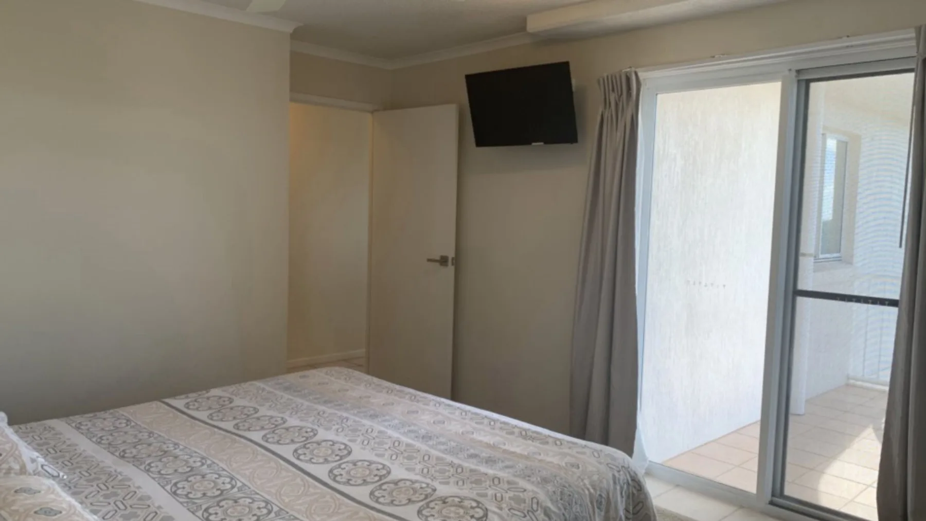 Un dormitorio con una colcha estampada, un televisor en la pared y puertas corredizas de vidrio.