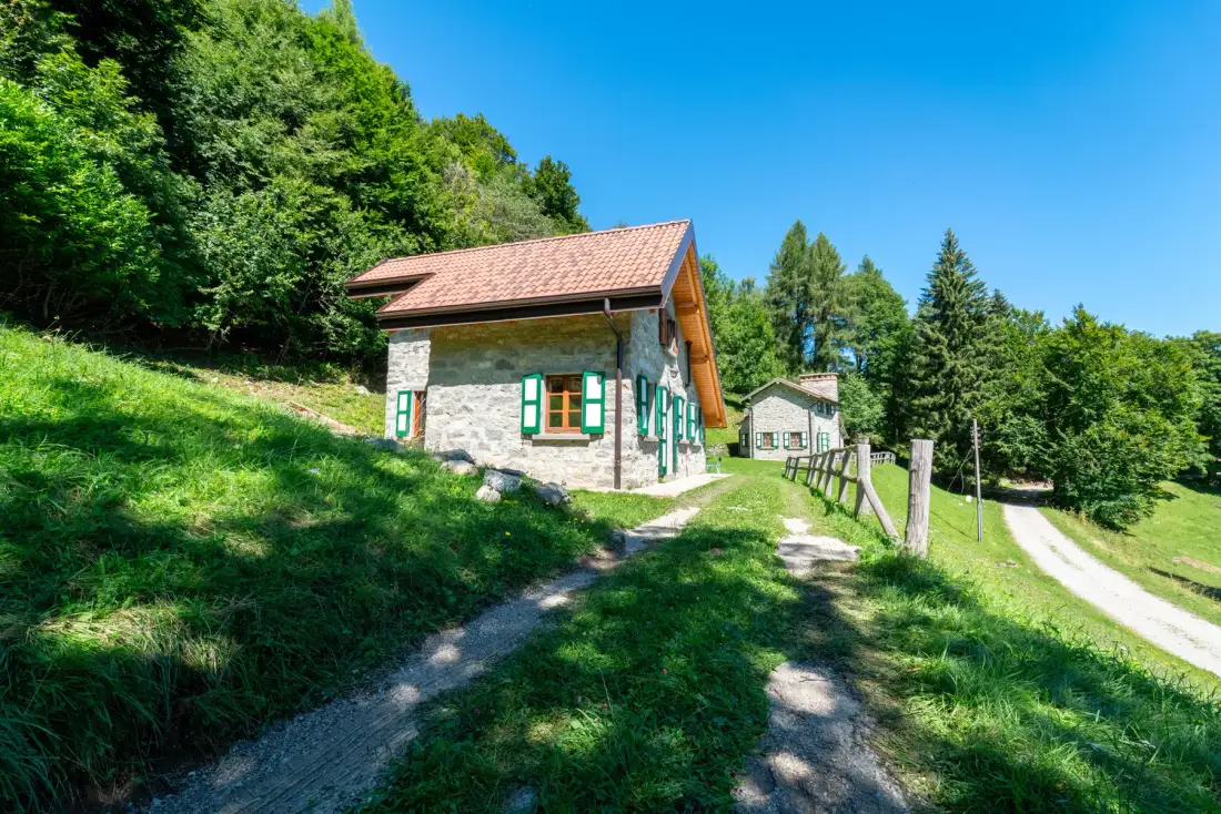 Una casa de piedra está junto a un sendero de grava en un entorno verde y arbolado.