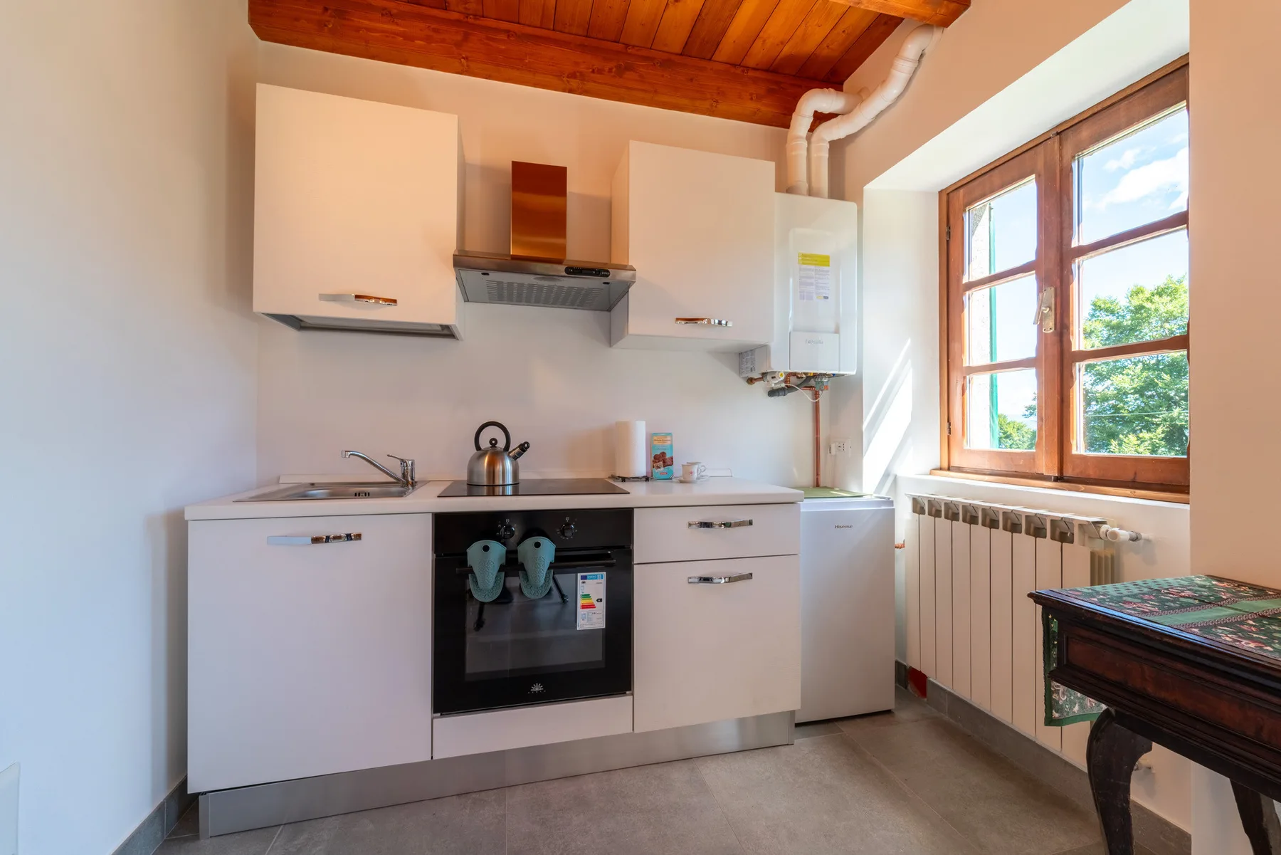 Una cocina compacta con armarios blancos, un horno empotrado y una ventana grande.