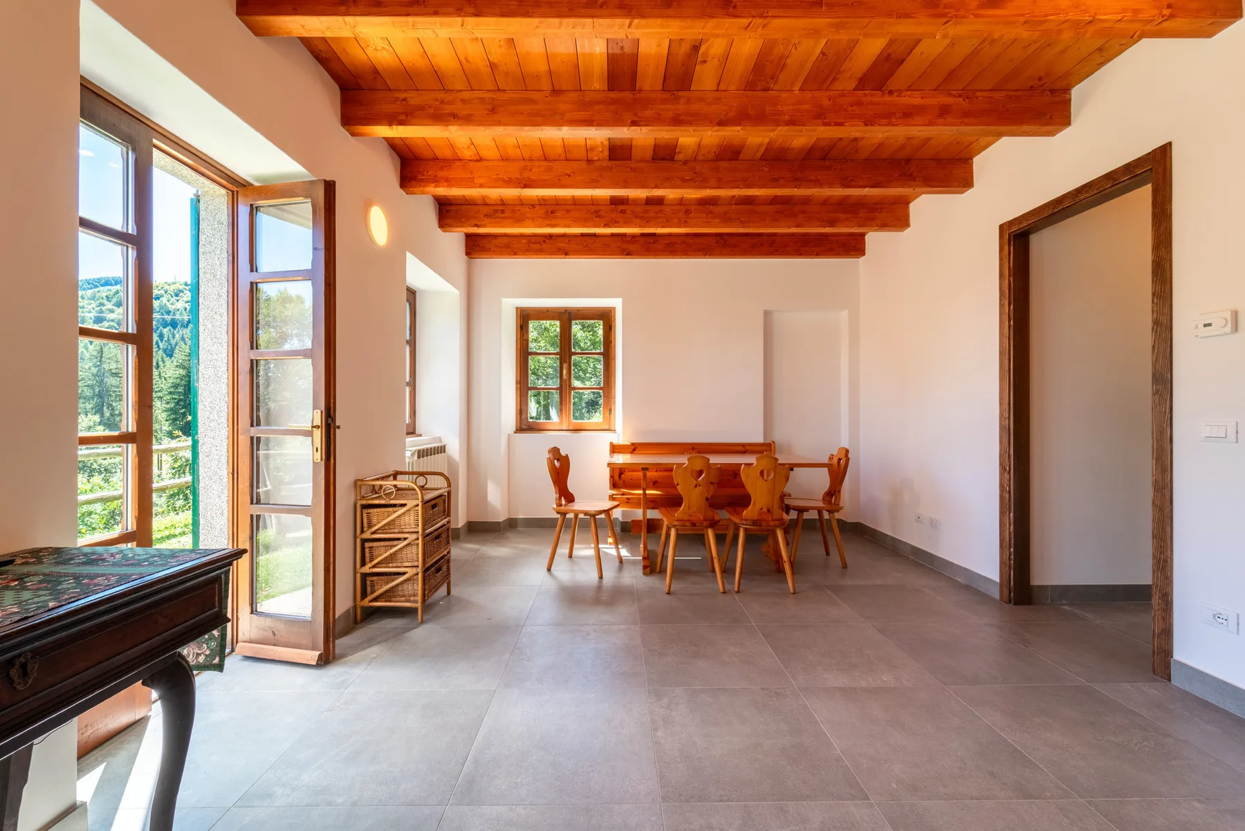 Comedor con mesa y sillas de madera bajo vigas de madera vistas en el techo.