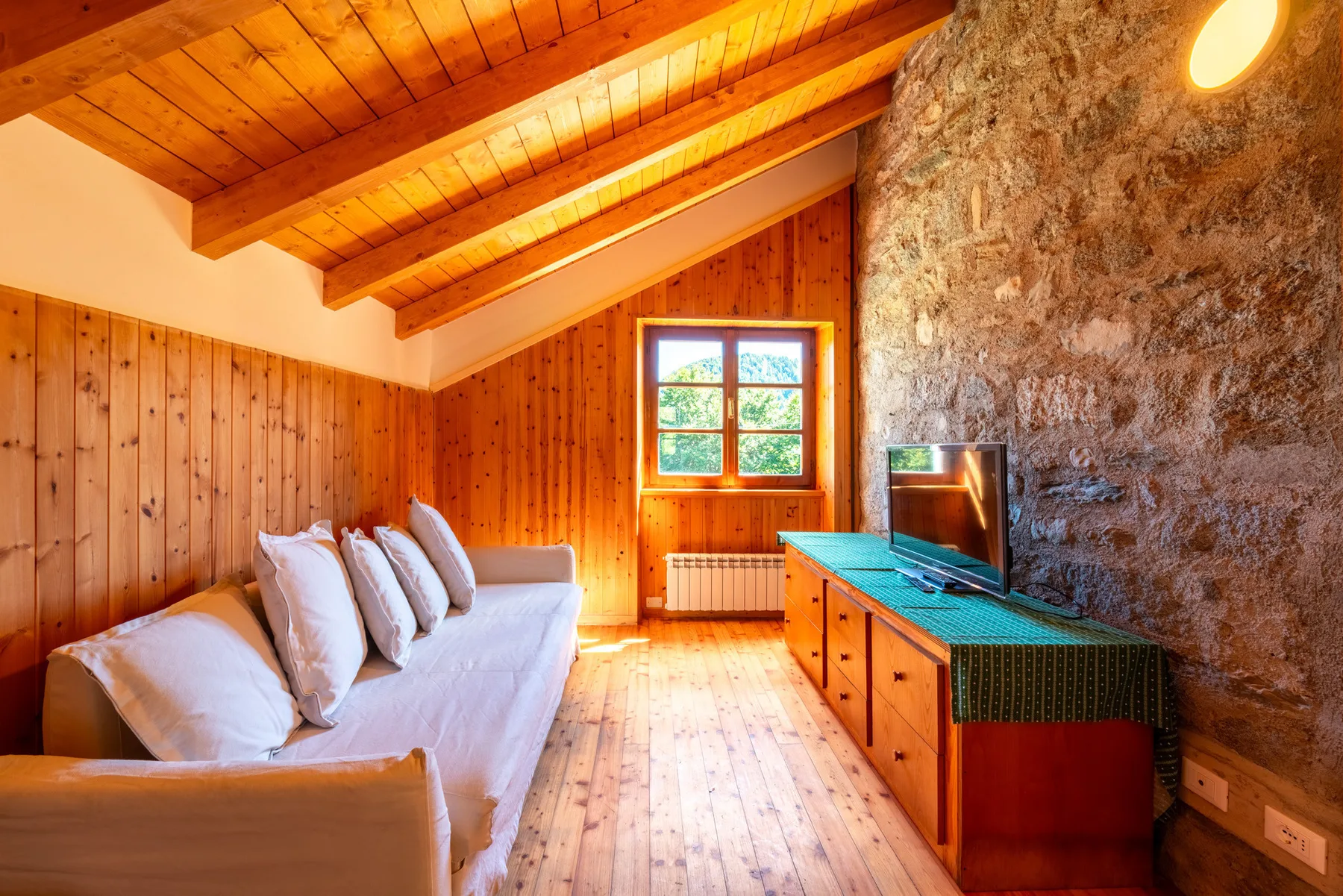 Un dormitorio revestido de madera con una cama junto a una pared de piedra y un televisor.
