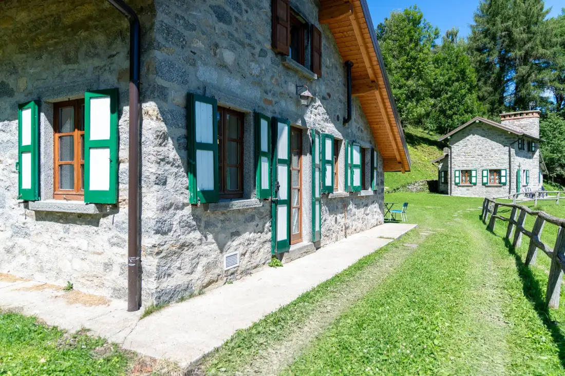 Una casa de piedra con contraventanas verdes está junto a un patio con césped.