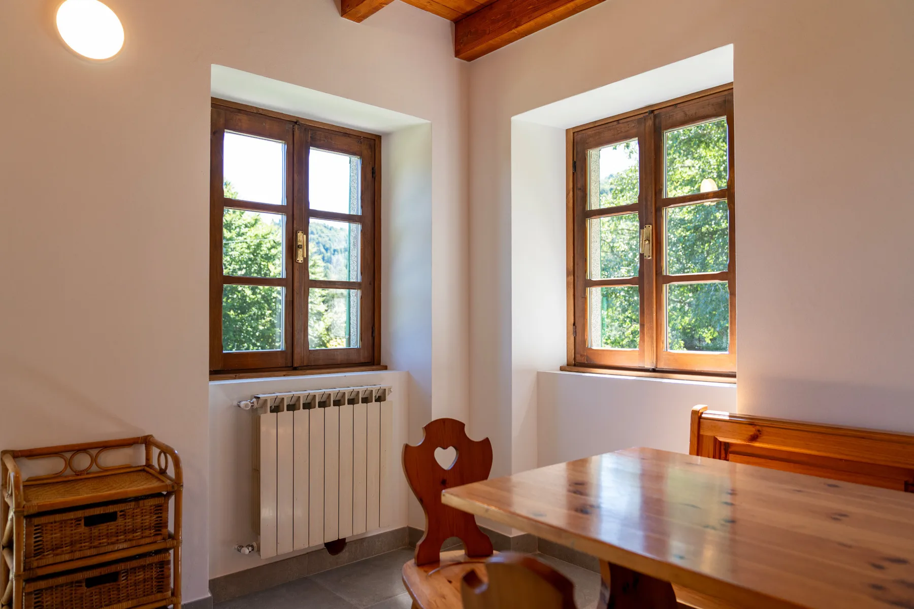 Una habitación luminosa con ventanas de marco de madera, un radiador y una mesa de madera.