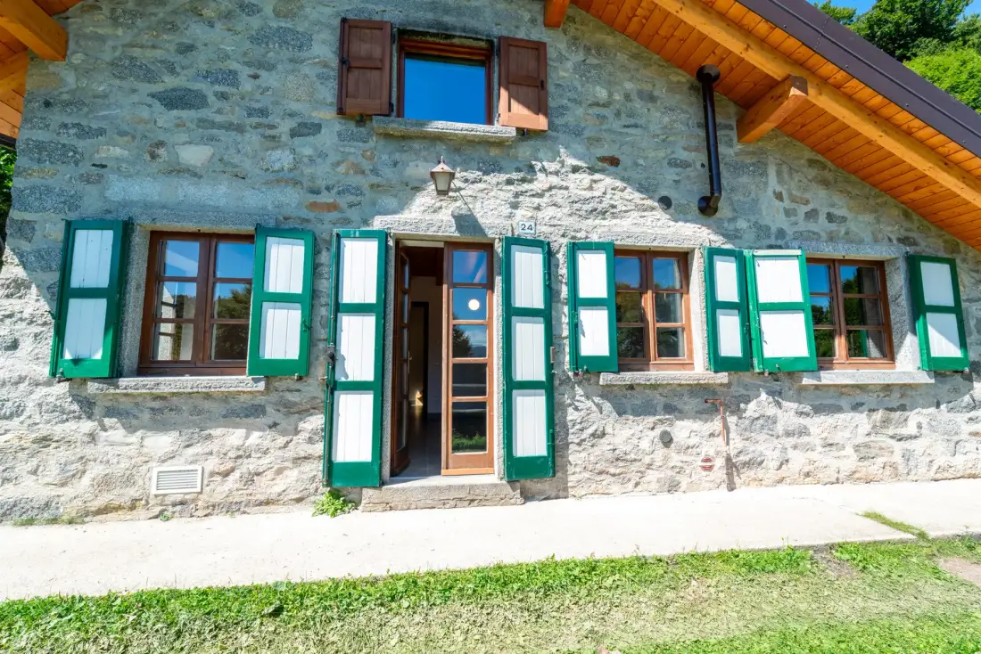 Exterior de una casa de piedra con contraventanas verdes y una puerta de entrada de madera.